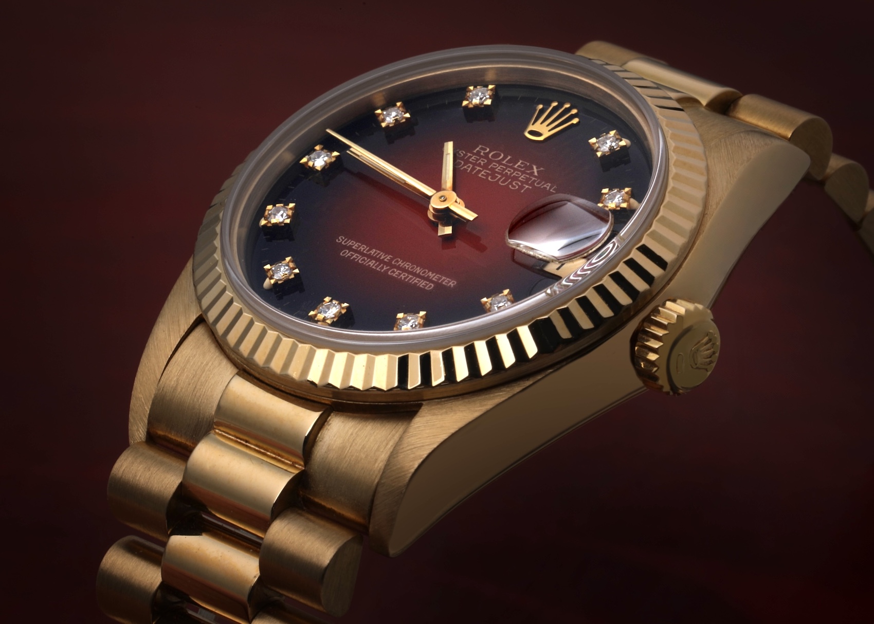 Close-up of a gold Rolex Datejust watch with a deep red vignette dial, diamond hour markers, and a fluted bezel, showcasing its Jubilee bracelet.