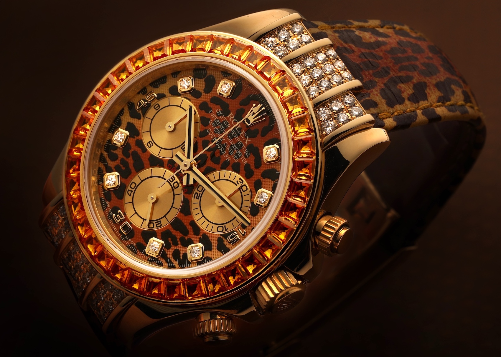Close-up of a striking gold Rolex Daytona 'Leopard' watch with a leopard print dial, diamond hour markers, orange sapphire bezel, and diamond-set lugs, paired with a matching leopard print strap.