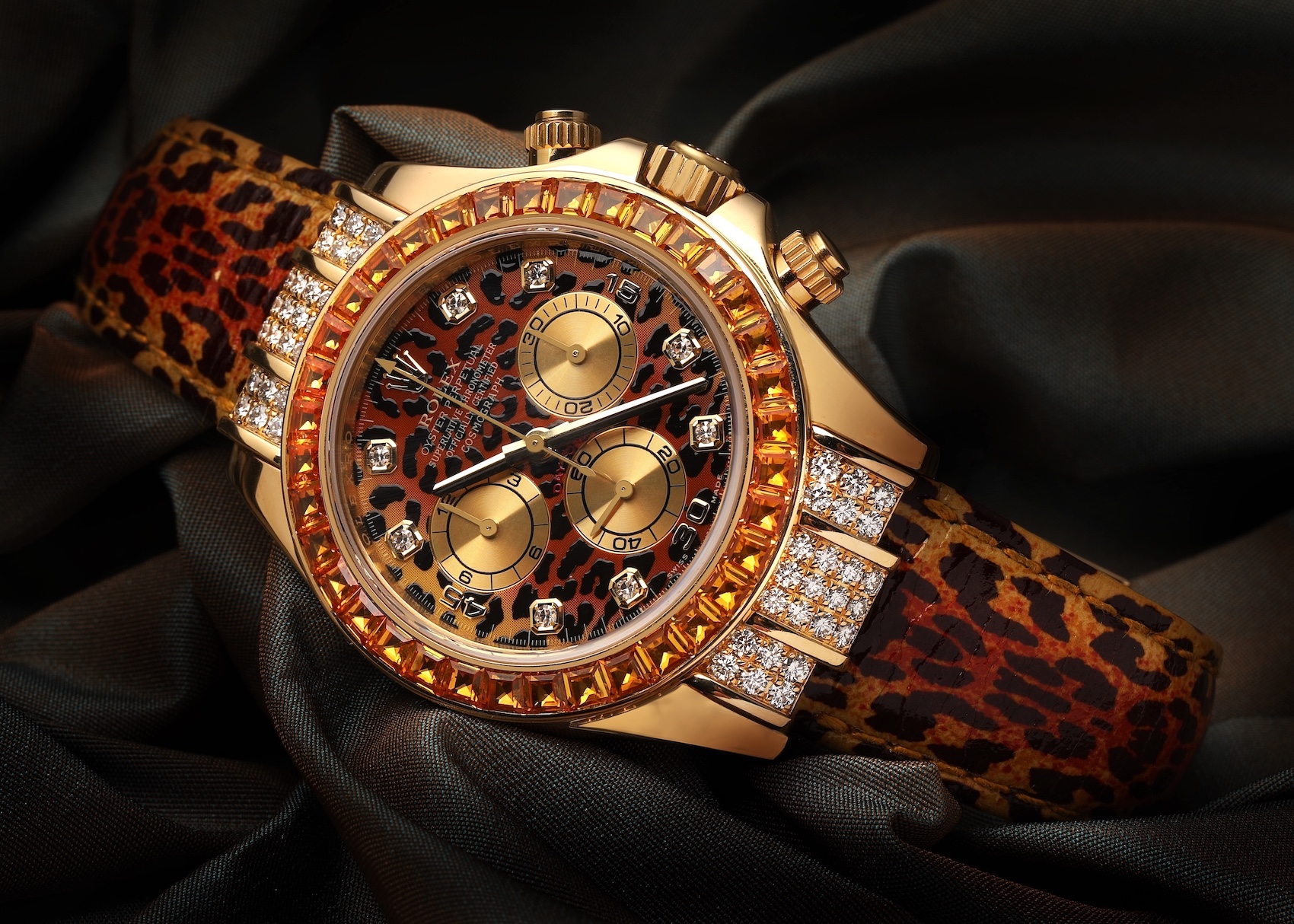 Close-up of a striking gold Rolex Daytona 'Leopard' watch with a leopard print dial, diamond hour markers, orange sapphire bezel, and diamond-set lugs, paired with a matching leopard print strap.