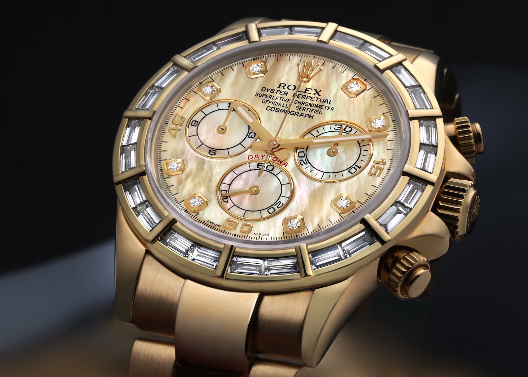 Close-up of a gold Rolex Daytona watch with a mother-of-pearl dial and diamond hour markers and baguette diamond bezel.