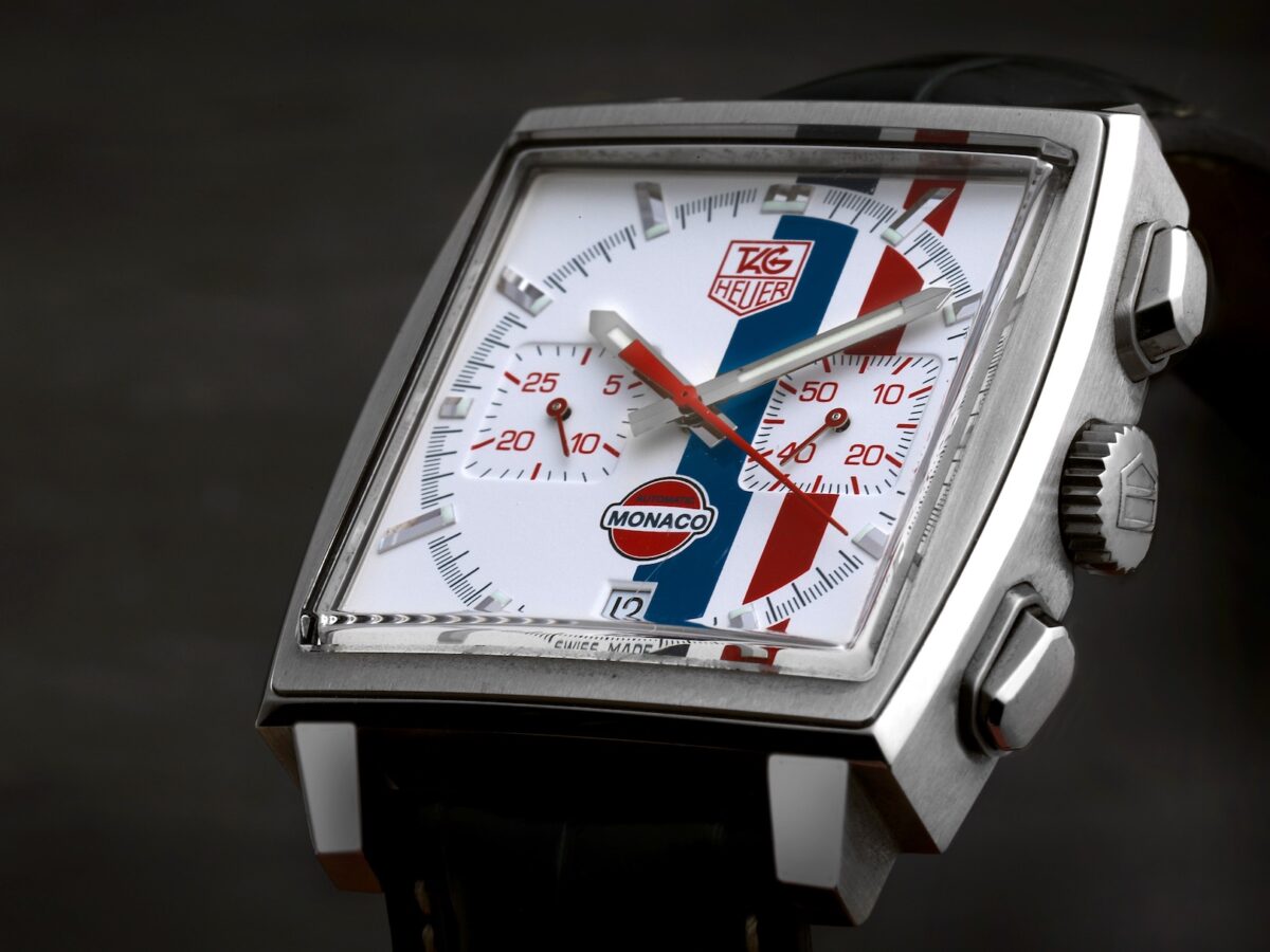 Detailed macro shot of the TAG Heuer Monaco Gulf CW2118 dial, highlighting the white face, red and blue vertical stripes, red chronograph hands, and applied hour markers.