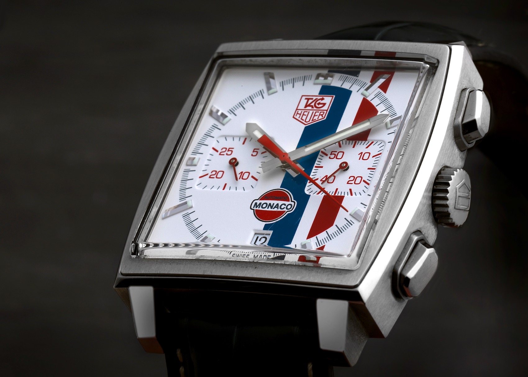 Detailed macro shot of the TAG Heuer Monaco Gulf CW2118 dial, highlighting the white face, red and blue vertical stripes, red chronograph hands, and applied hour markers.