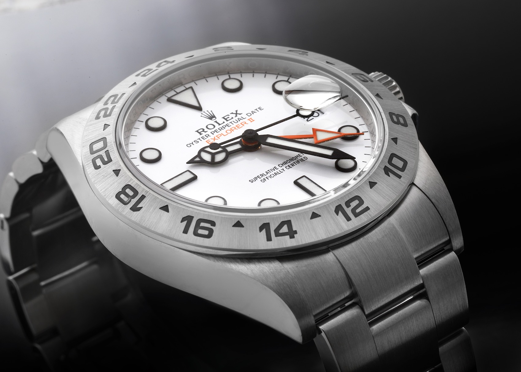 Close-up of a Rolex Explorer II "Polar" watch with a white dial, black hour markers, and an orange 24-hour hand, set against a dark background.