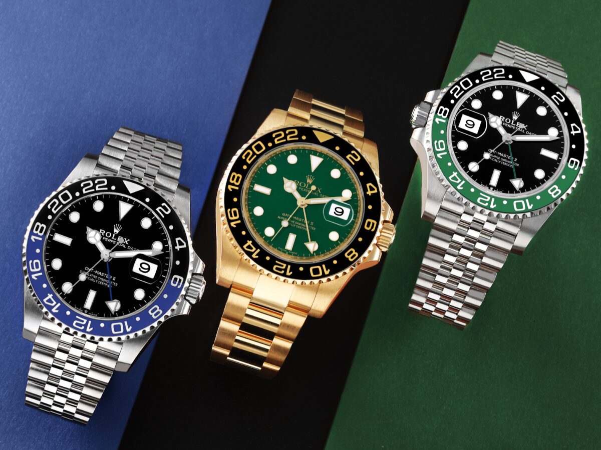 A top-down view of three iconic Rolex GMT-Master II watches: 'Pepsi' (red/blue), 'Sprite' (green/black), and a yellow gold GMT-Master II with a green dial.