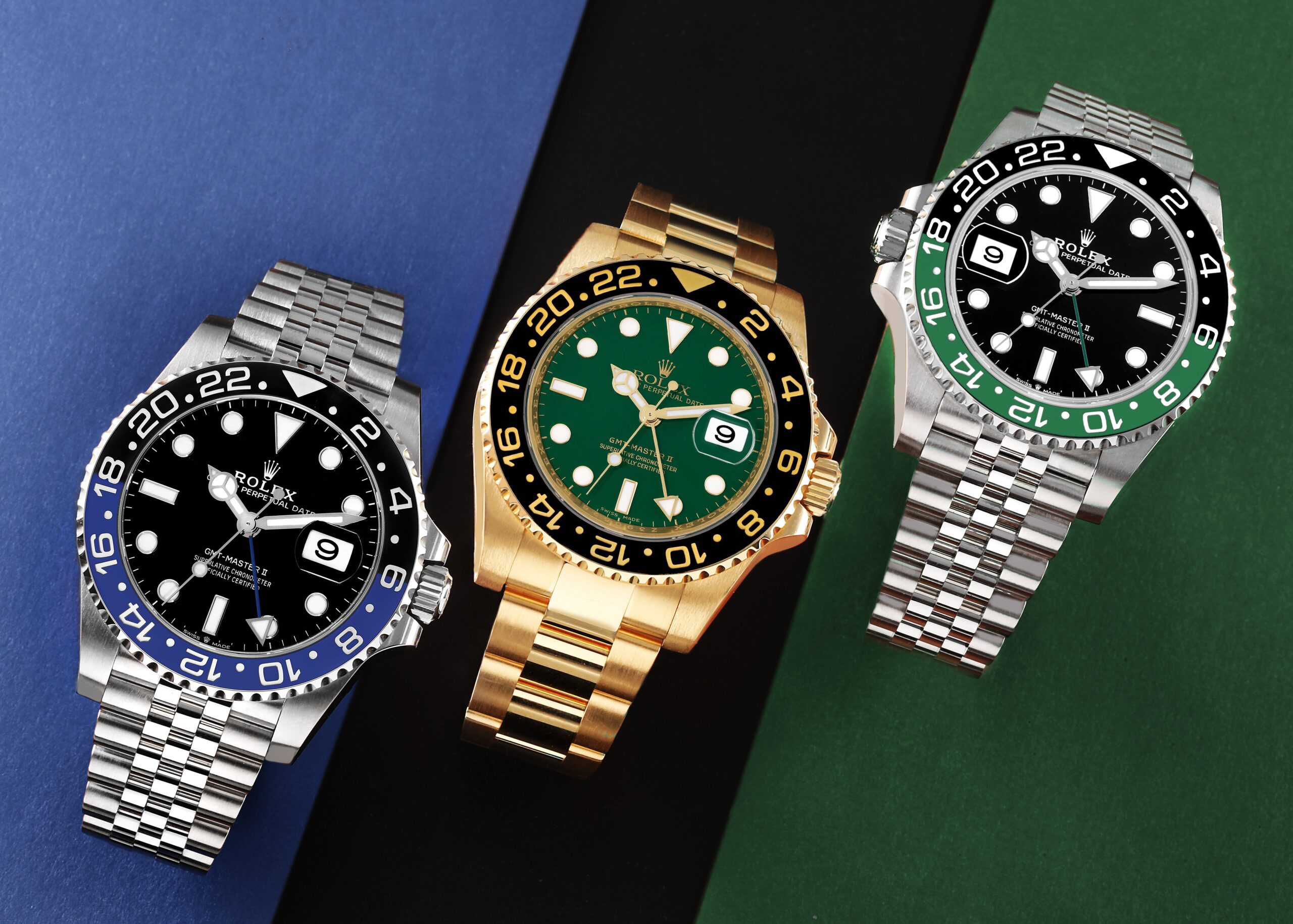 A top-down view of three iconic Rolex GMT-Master II watches: 'Pepsi' (red/blue), 'Sprite' (green/black), and a yellow gold GMT-Master II with a green dial.
