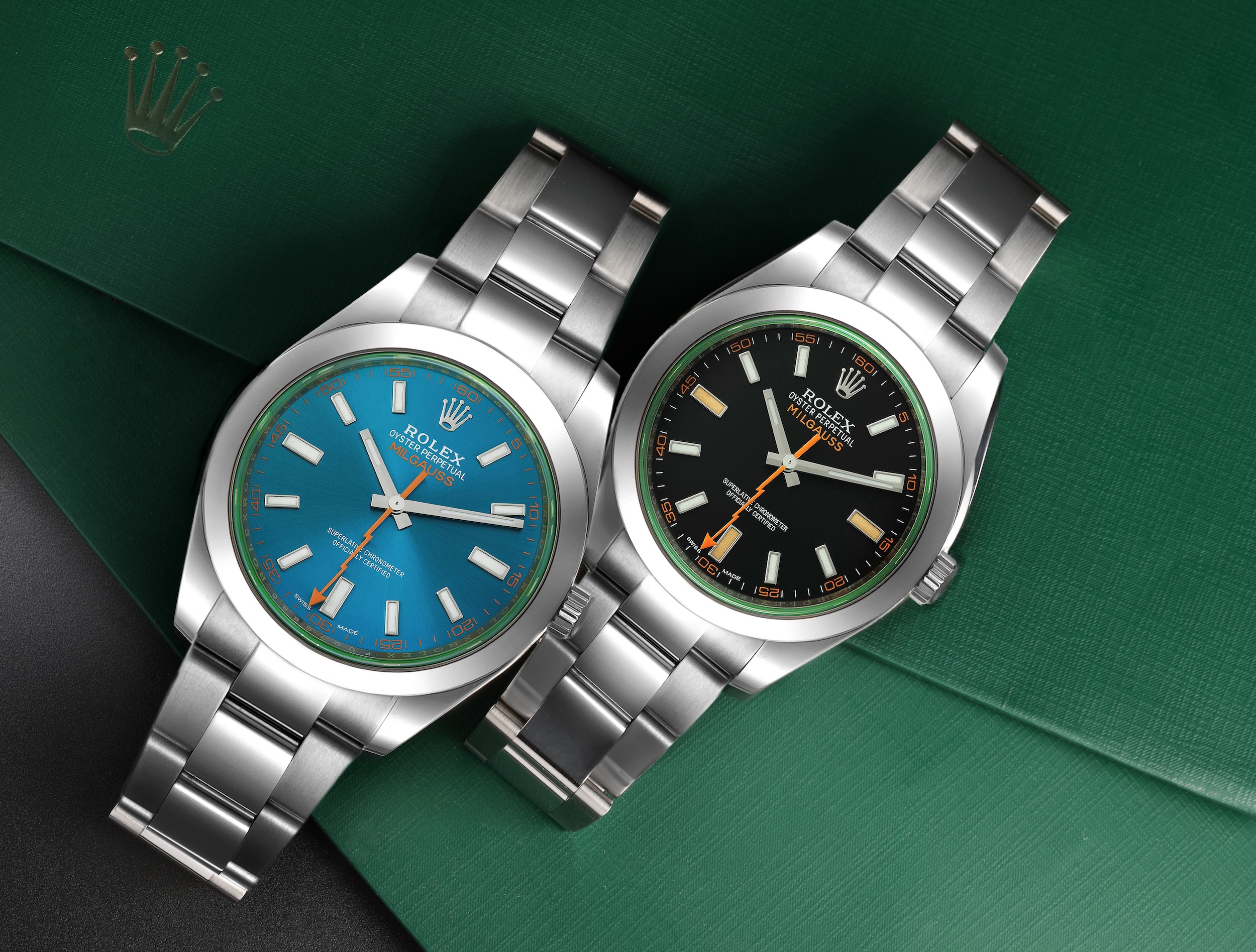 Two Rolex Milgauss watches, one with a 'Z-Blue' electric blue dial and the other with a black dial, both featuring green sapphire crystals and orange lightning bolt seconds hands.