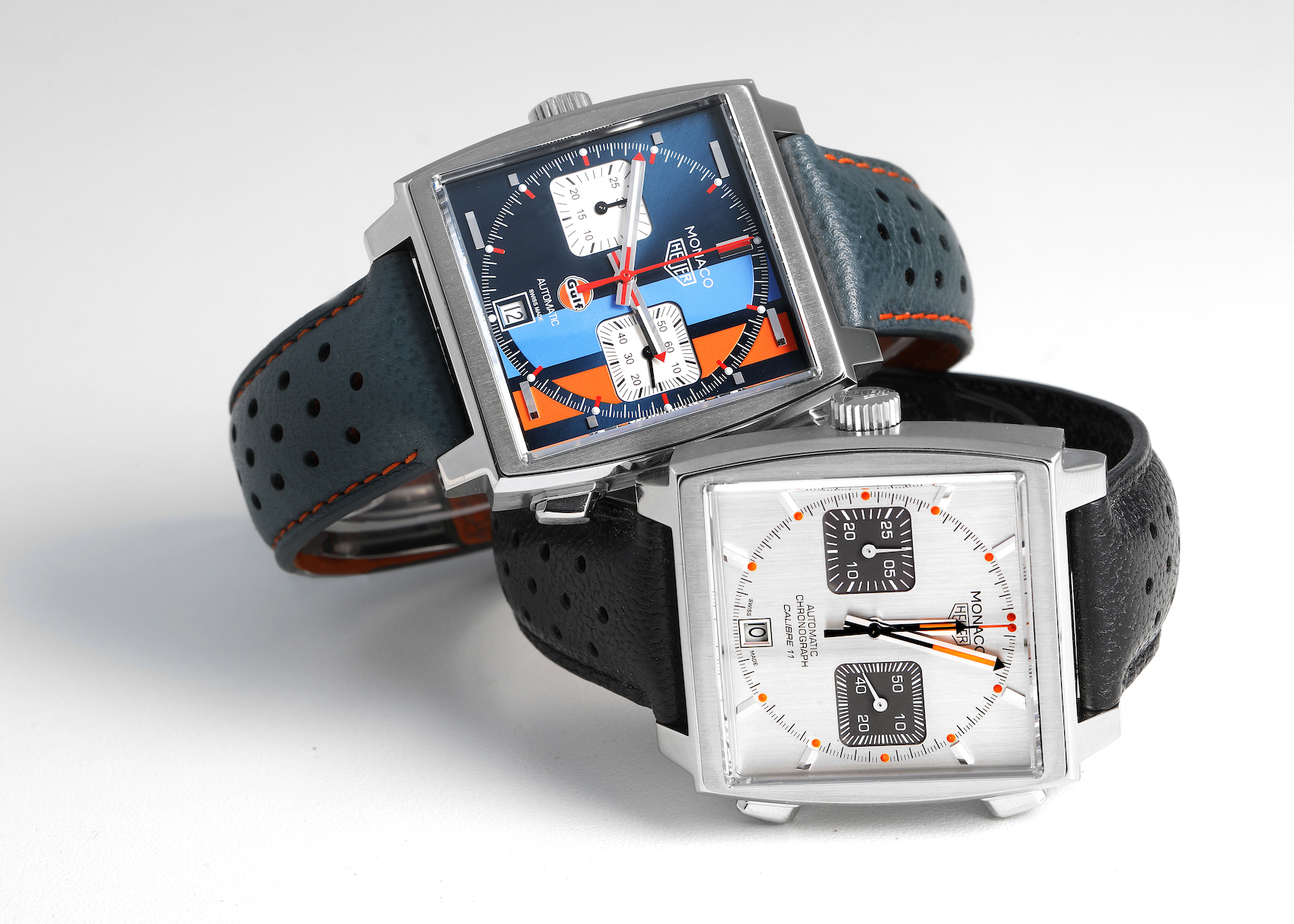 The blue dial TAG Heuer Monaco Gulf CAW211R watch resting on top of a white dial TAG Heuer Monaco, showcasing their contrasting designs against a clean white background.