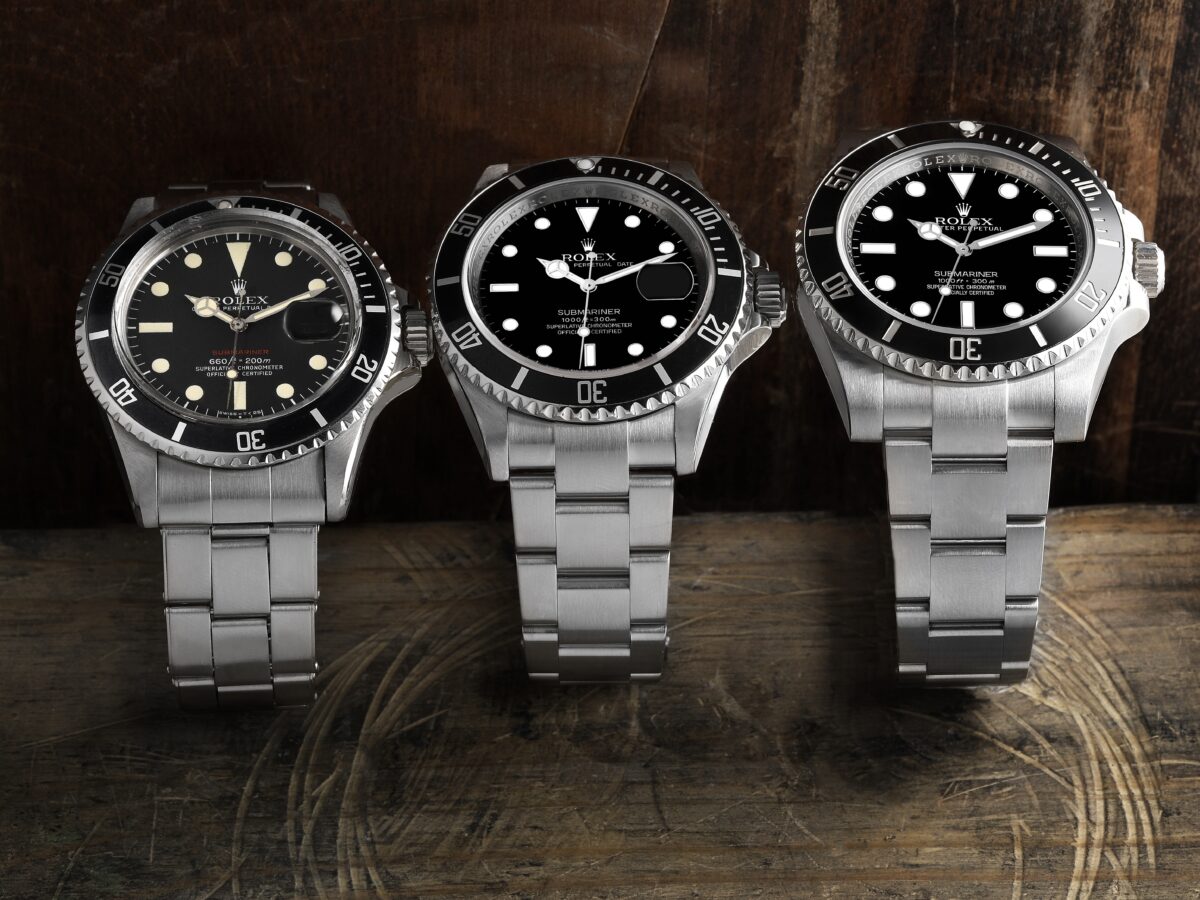 A comparison of three Rolex Submariner models. On the left, a vintage model with a date window; in the center, a pre-ceramic model; and on the right, the modern ceramic Submariner ref. 114060.