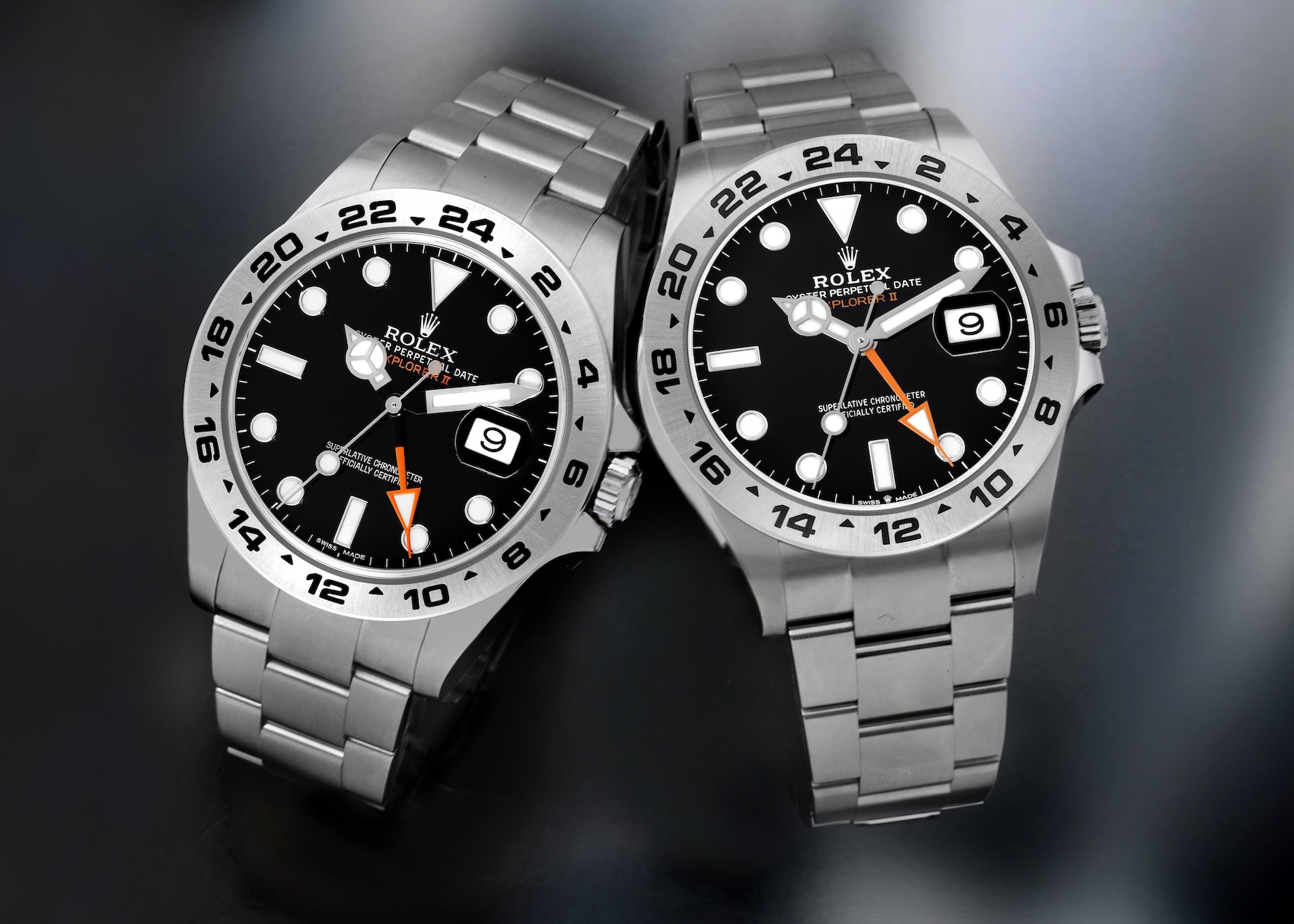 Two stainless steel Rolex Explorer II watches are shown side-by-side on a dark surface: on the left, the older reference 216570 with a 42mm case, and on the right, the newer reference 226570 with subtle refinements to the case and bracelet. Both feature black dials, white luminous markers, orange 24-hour hands, and fixed 24-hour bezels.