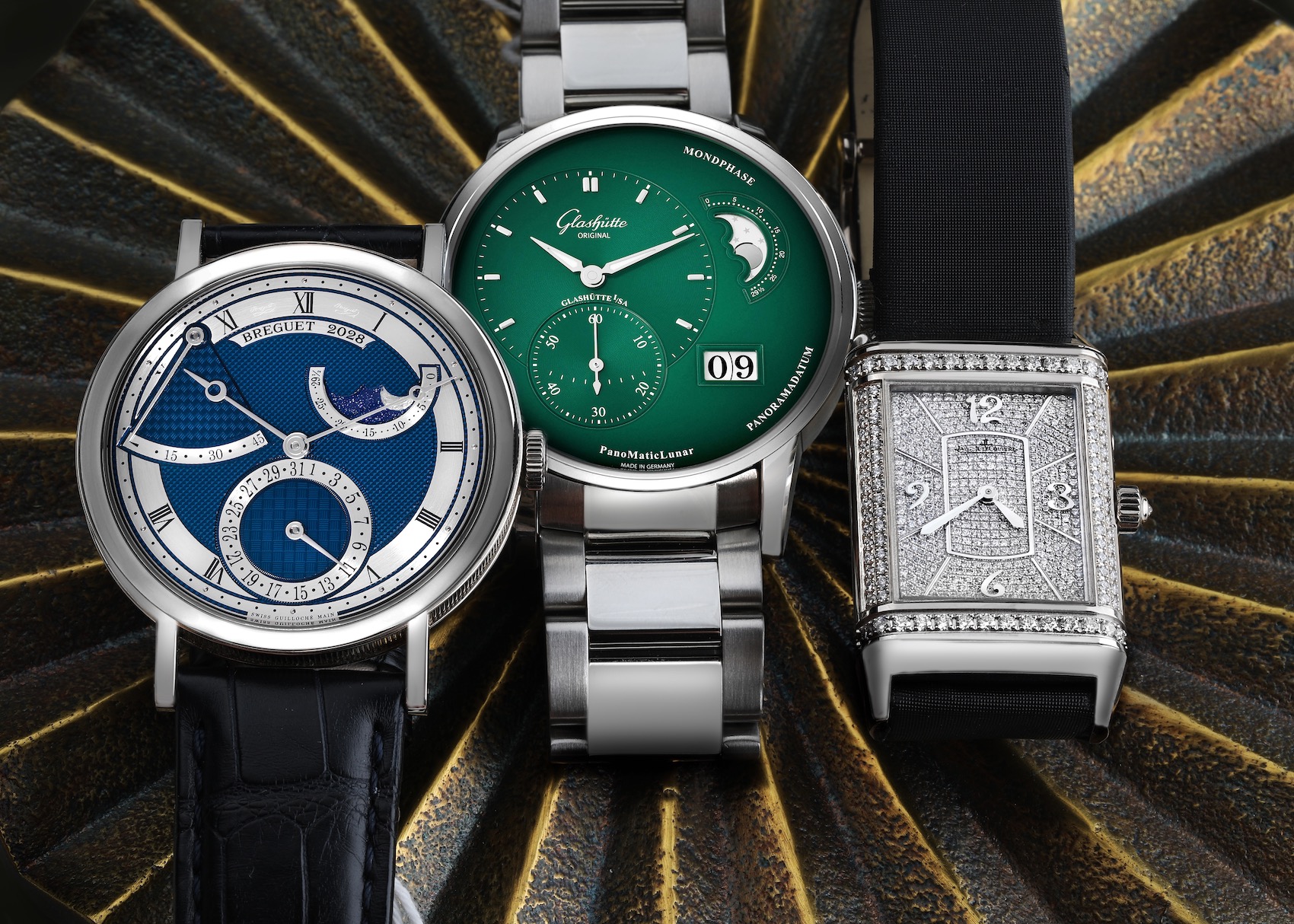 Three unique luxury dress watches: a Breguet Classique with a blue guilloché dial, a Glashutte Original PanomaticLunar with a vibrant green dial, and a Jaeger-LeCoultre Reverso with a full diamond-pavé dial.