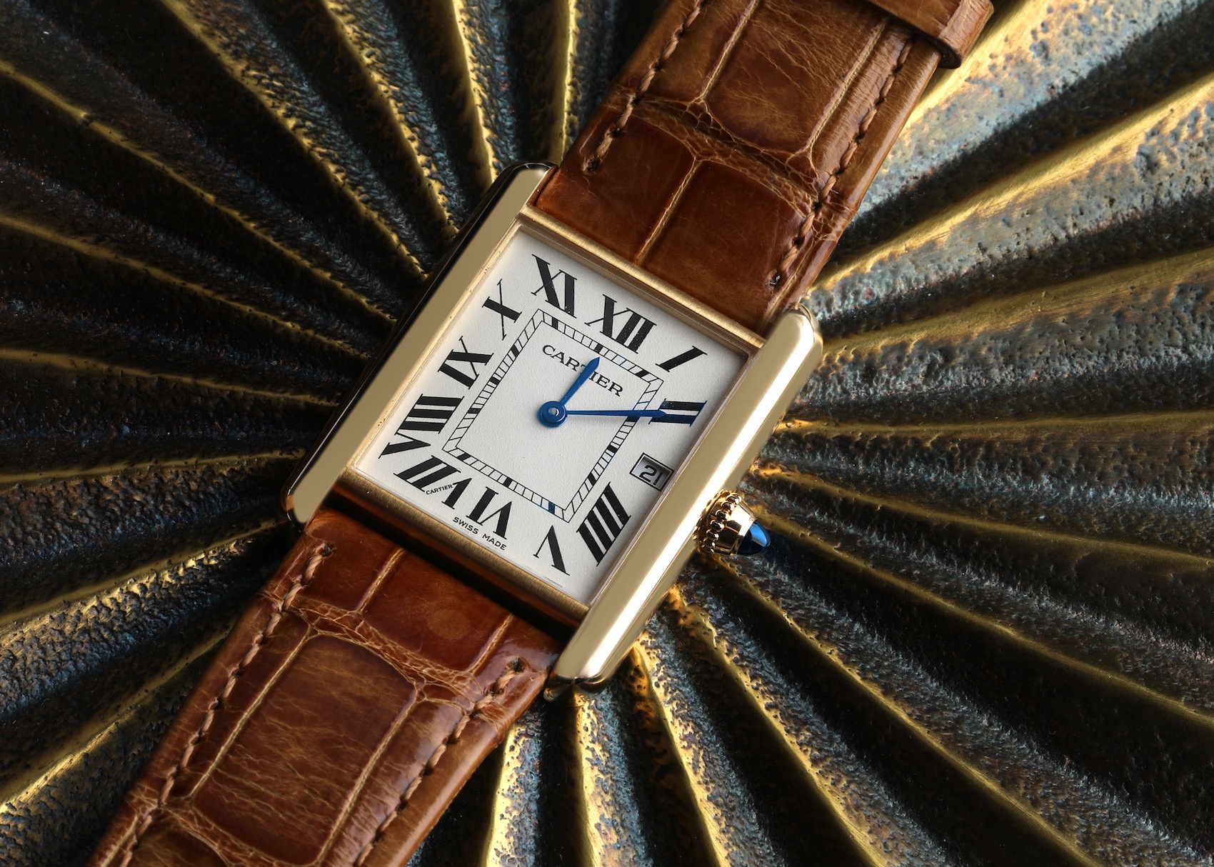 A detailed close-up of a classic Cartier Tank Louis watch in yellow gold, featuring a white dial with black Roman numerals and a brown alligator leather strap.