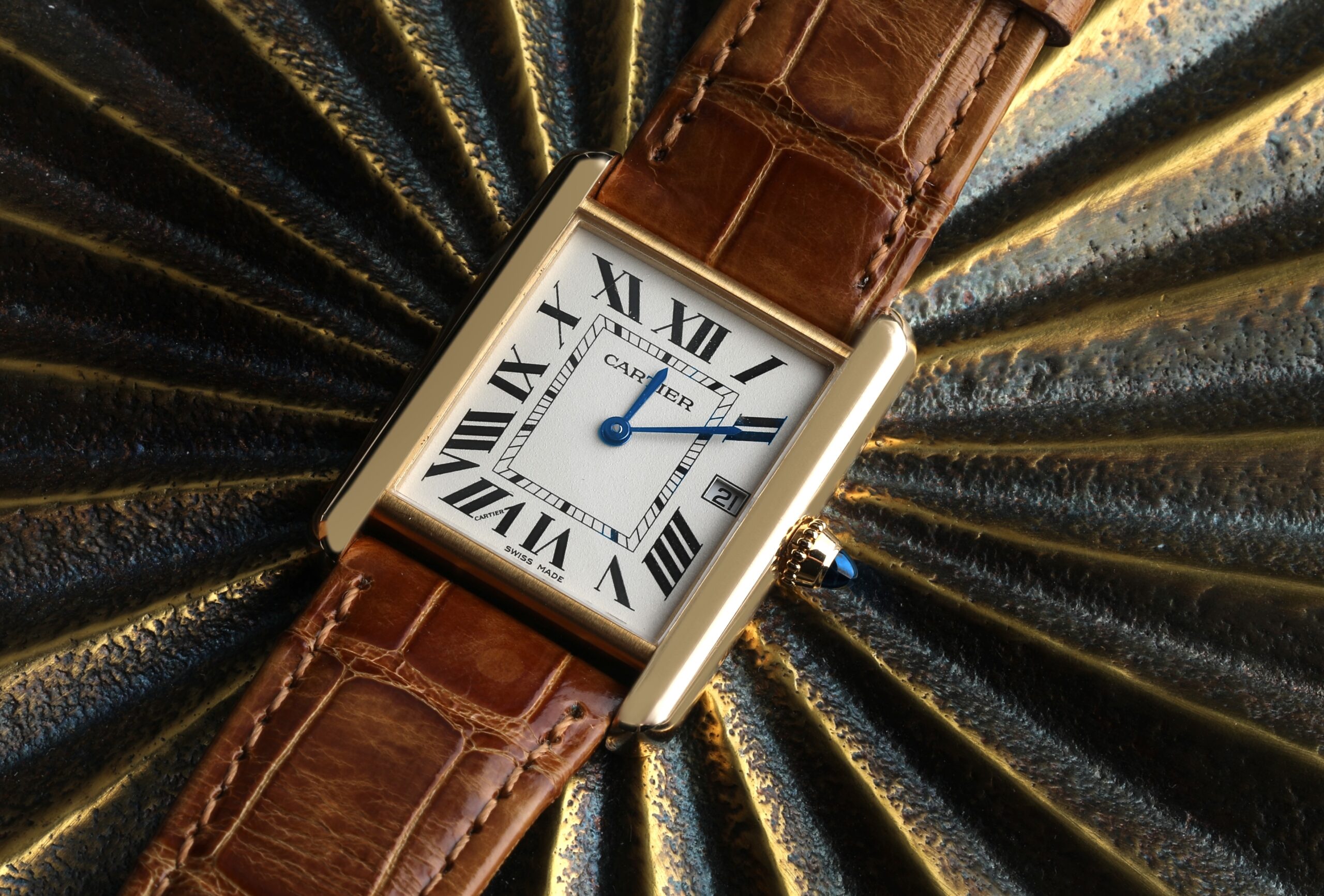Close-up of a classic Cartier Tank Louis watch in yellow gold, with its signature Roman numeral dial and blue steel hands on a brown leather strap.