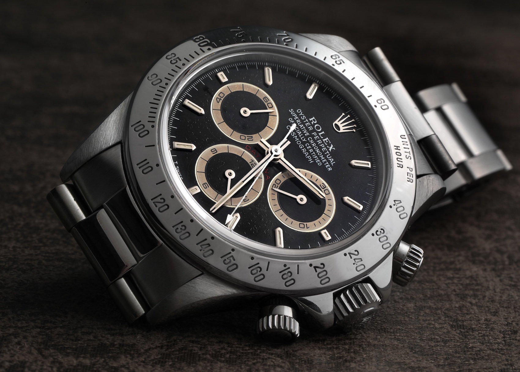 A stainless steel Rolex Daytona reference 16520 with a black dial and contrasting subdials, featuring a tachymeter bezel and chronograph pushers, is positioned on a textured surface.