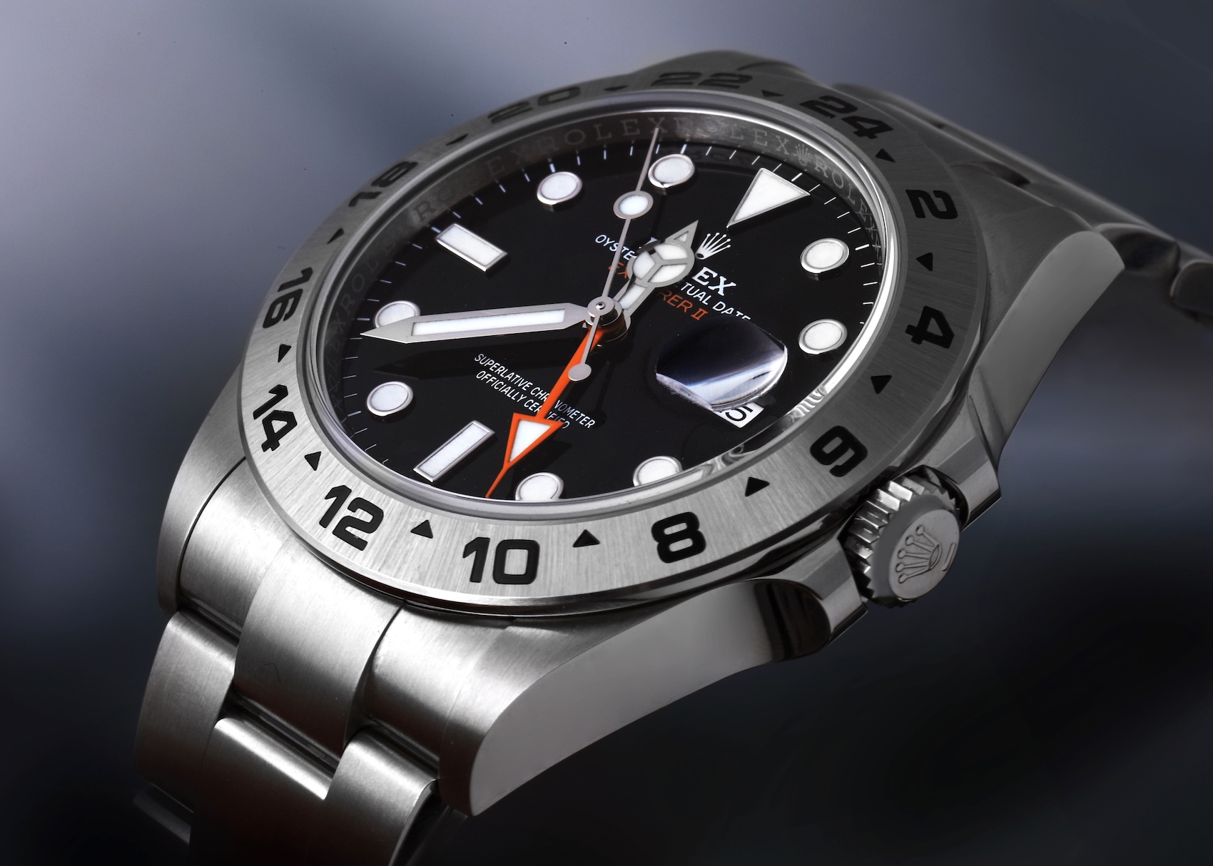 A detailed, angled shot of a stainless steel Rolex Explorer II 216570 showcases its black dial, prominent white indices, the signature bright orange 24-hour hand, and the brushed stainless steel bezel with engraved 24-hour markings.