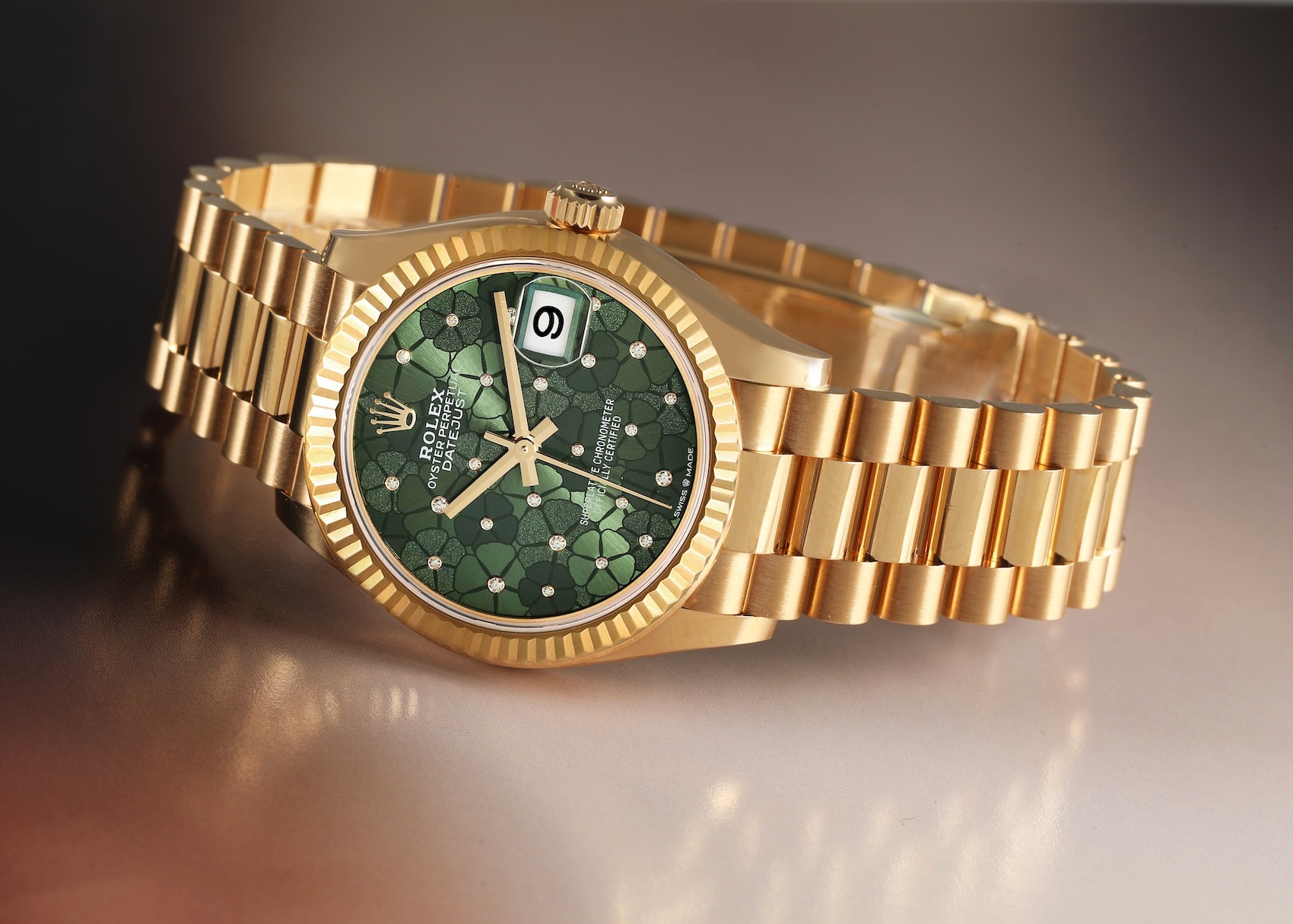 A yellow gold Rolex Lady-Datejust 278278 is showcased, featuring a striking green floral motif dial adorned with diamonds, a fluted bezel, and a President bracelet.
