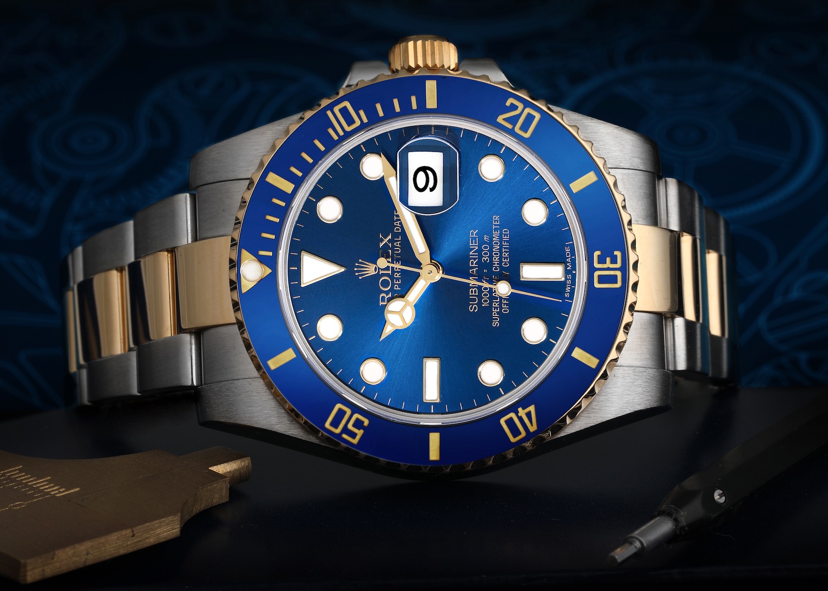  A stunning Rolex Submariner 116613 is showcased, featuring a vibrant blue ceramic bezel, a matching blue sunburst dial with gold accents, and a two-tone steel and yellow gold Oyster bracelet.