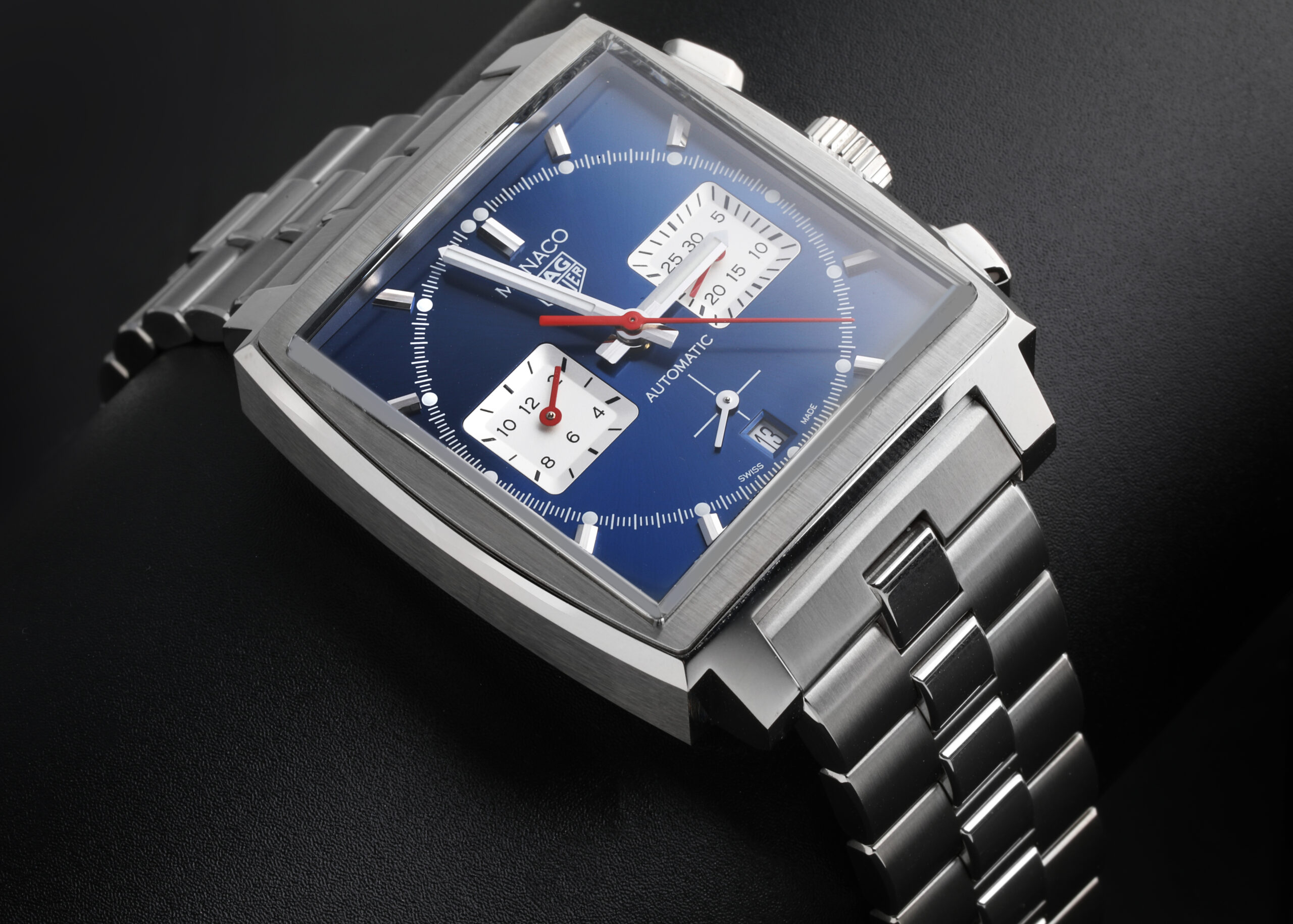 Angled view of the iconic square-cased TAG Heuer Monaco watch, featuring a vibrant blue dial with square sub-dials and a red chronograph hand.