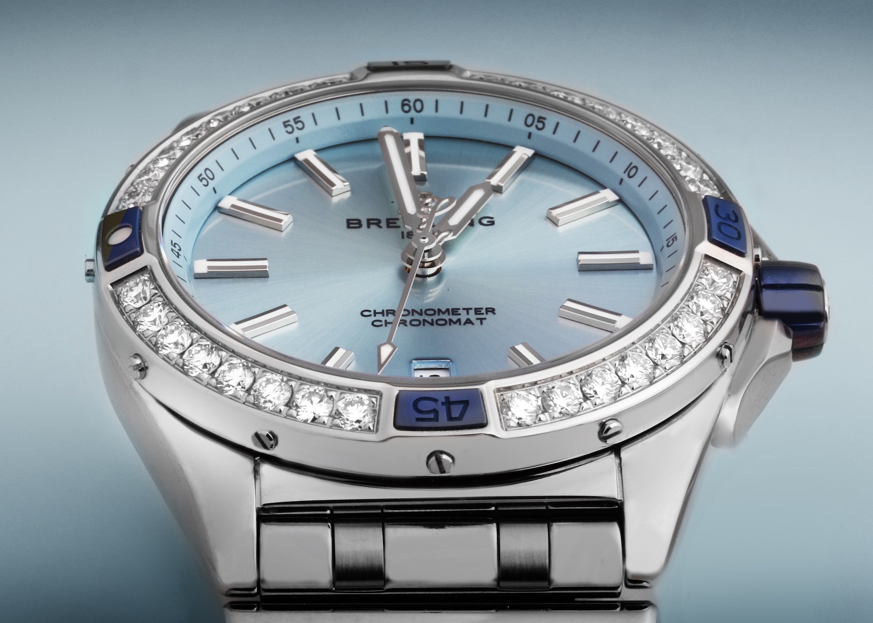 A detailed shot of the Breitling Super Chronomat for women, highlighting its diamond-studded bezel, light blue sunray dial, and distinctive rider tabs with blue ceramic accents.
