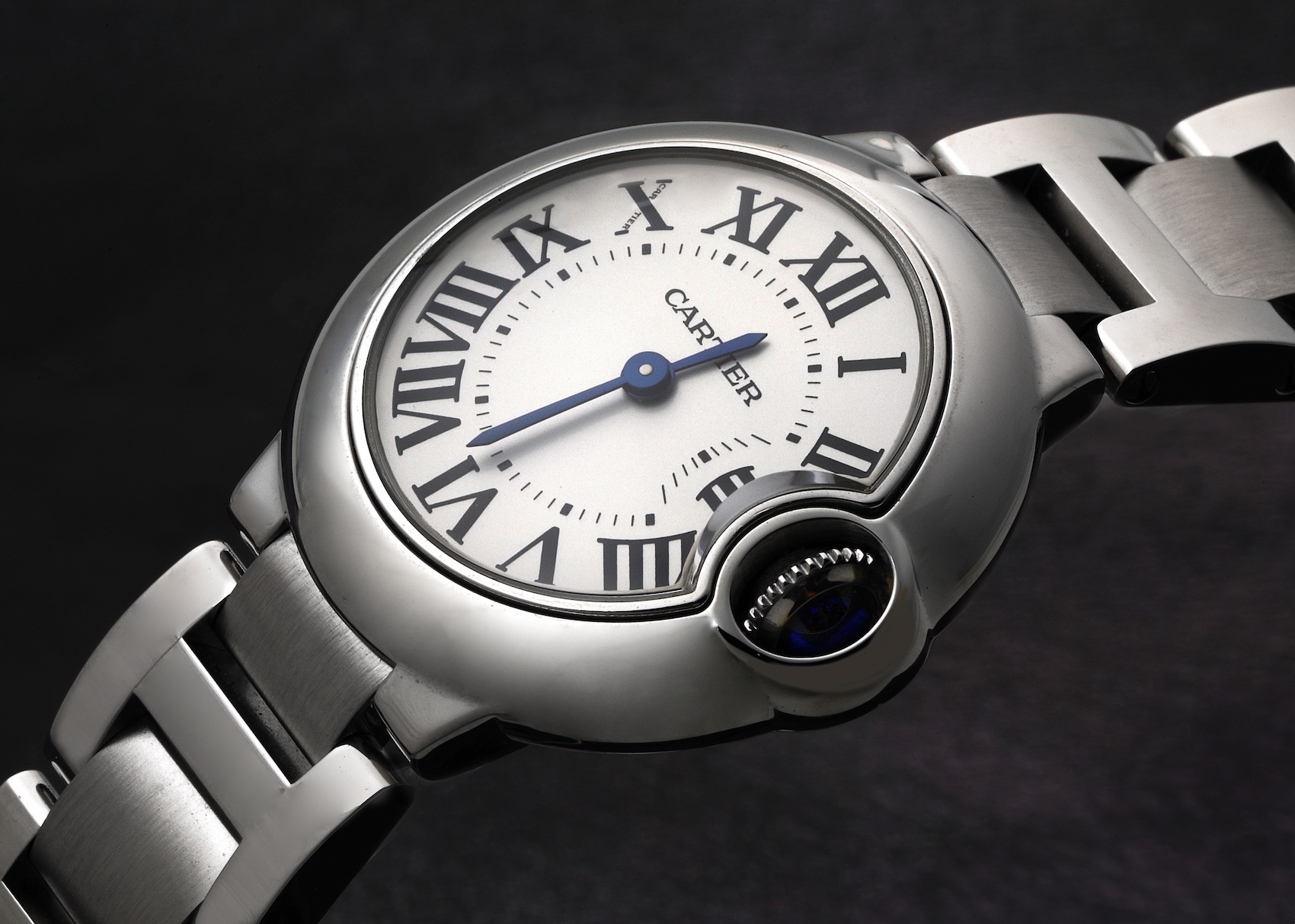 A close-up of the Cartier Ballon Bleu ladies' watch, featuring a silver steel case, a white dial with black Roman numerals, blued-steel hands, and its signature protected crown.