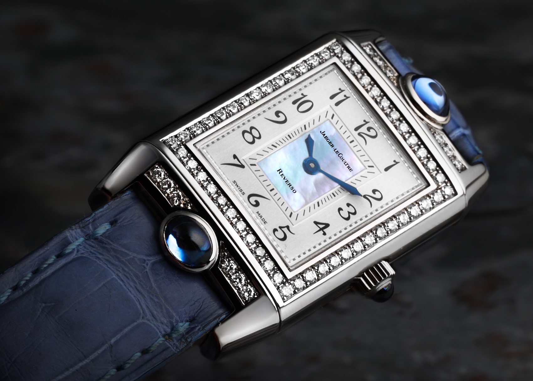 A Jaeger-LeCoultre Reverso Joaillerie ladies' watch, showcasing its rectangular diamond-set white gold case, a delicate mother-of-pearl dial, and a rich blue alligator strap.