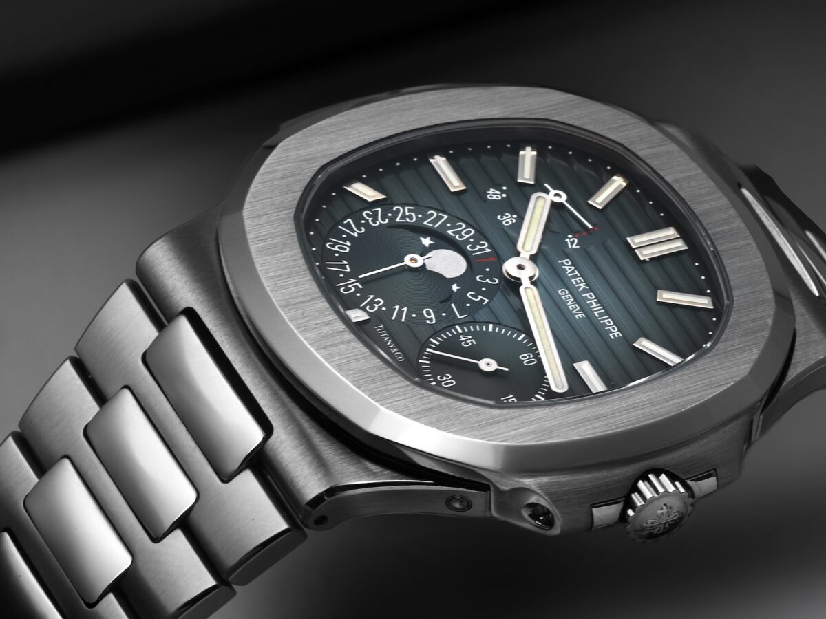 Angled shot of a Patek Philippe Nautilus 5712/1A with a Tiffany & Co. co-branded dial. The watch features its iconic stainless steel octagonal case, a horizontally embossed gray-blue dial with moonphase and power reserve indicators, and an integrated steel bracelet.