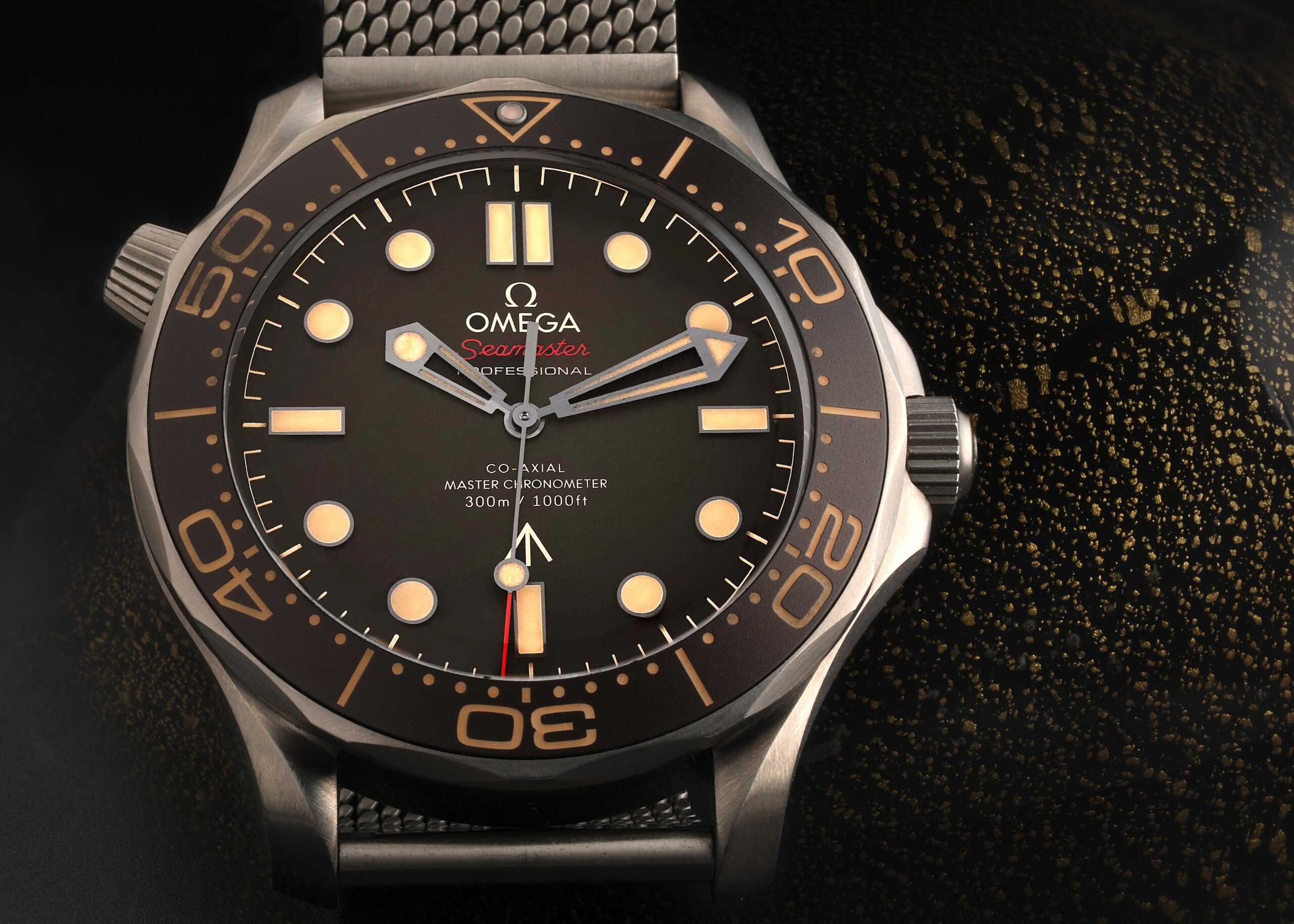 A detailed macro shot of the OMEGA Seamaster 007 Edition 'No Time to Die' watch, highlighting its titanium case and matte tropical brown dial.