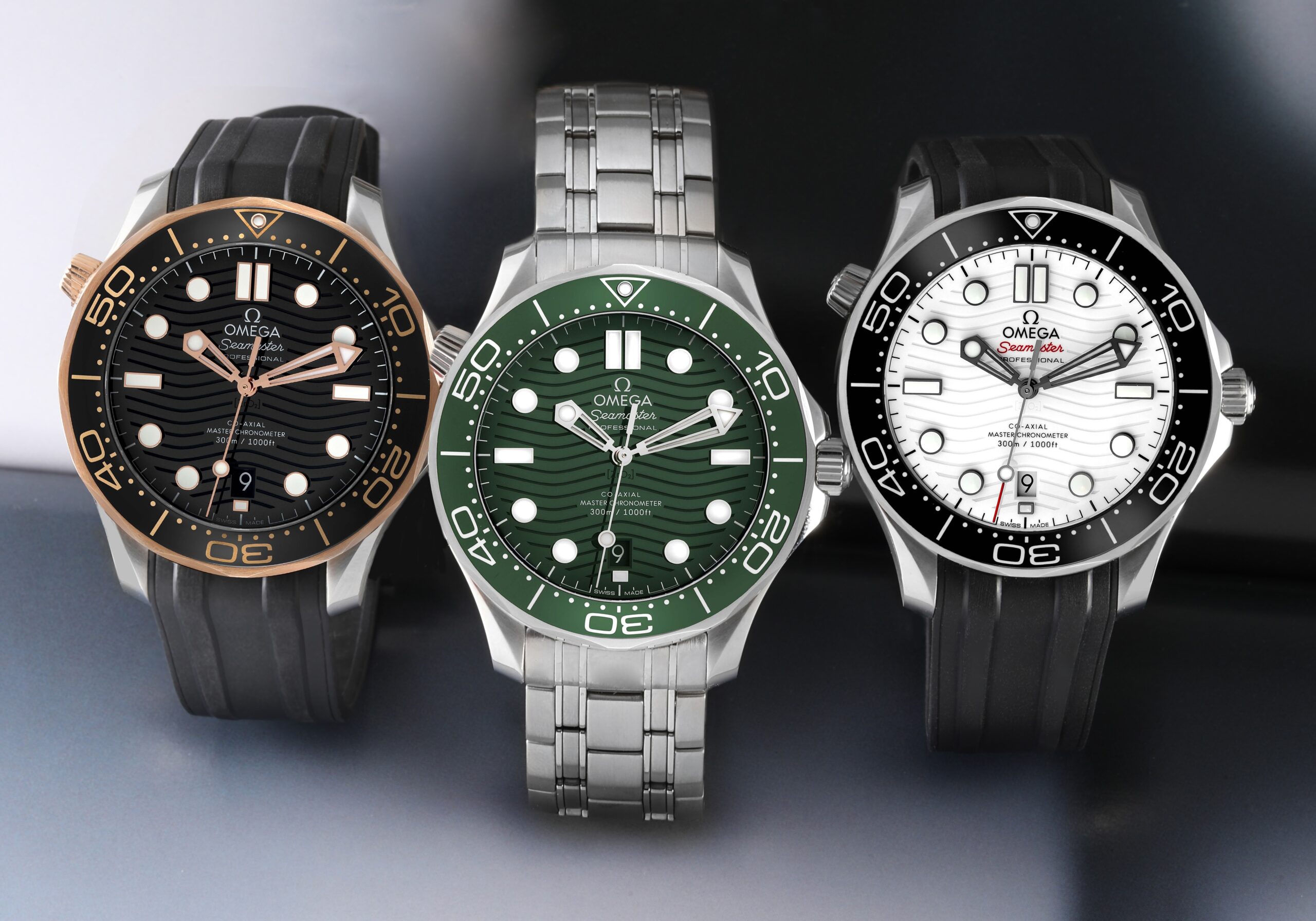A group photo of three modern OMEGA Seamaster Diver 300M watches in black and gold, green steel, and white steel variations.