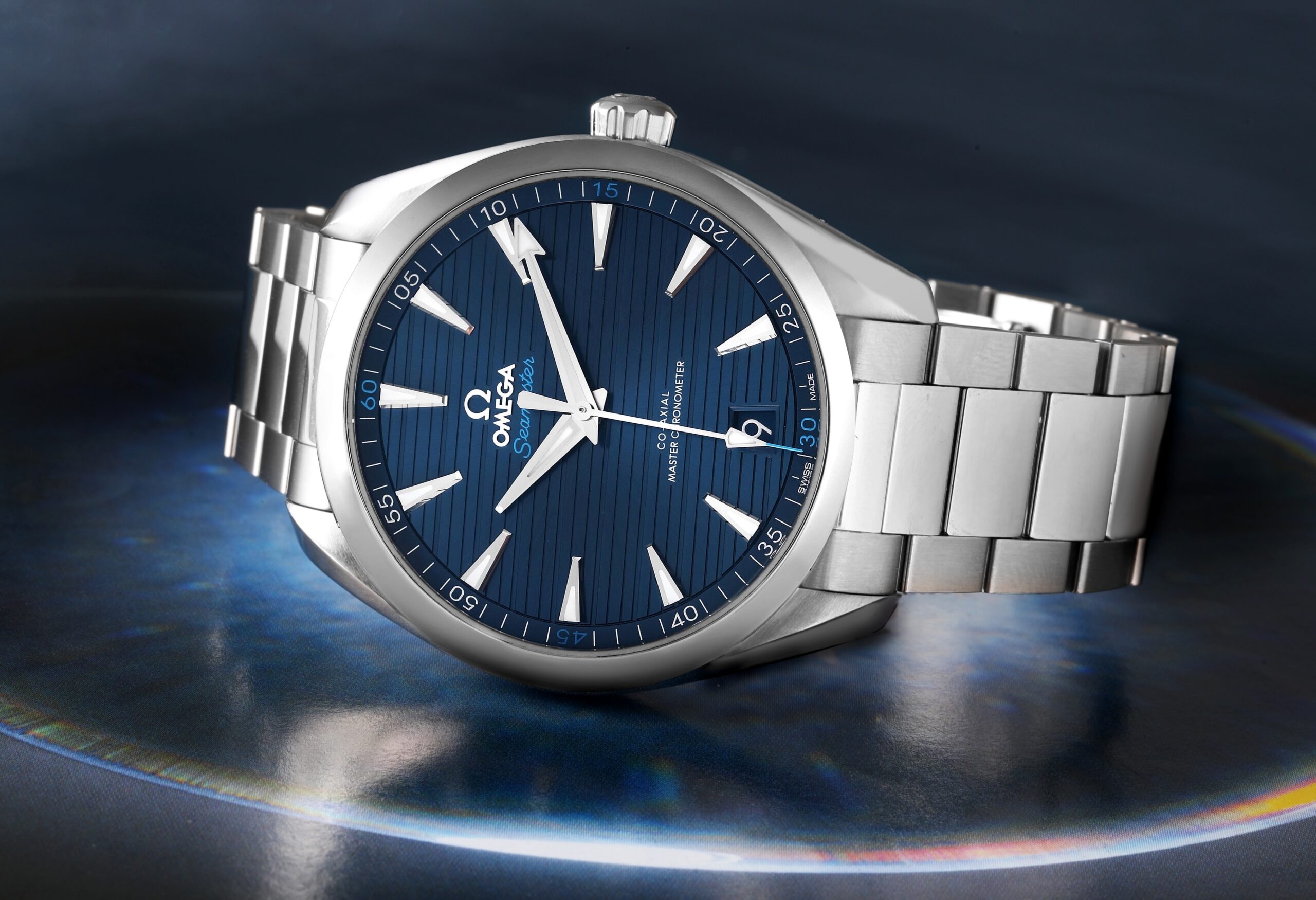 A steel OMEGA Seamaster Aqua Terra watch with a blue teak-pattern dial, angled to show its polished case and bracelet.