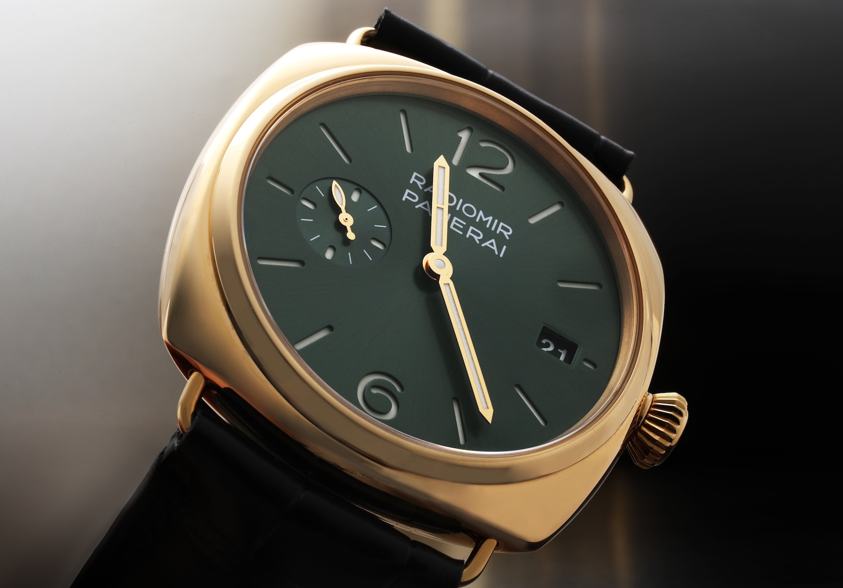 Close-up of a Panerai Radiomir Quaranta watch in yellow gold. It has a cushion-shaped case, a sun-brushed green dial with a small seconds subdial at 9 o'clock, and is fitted with a black leather strap.