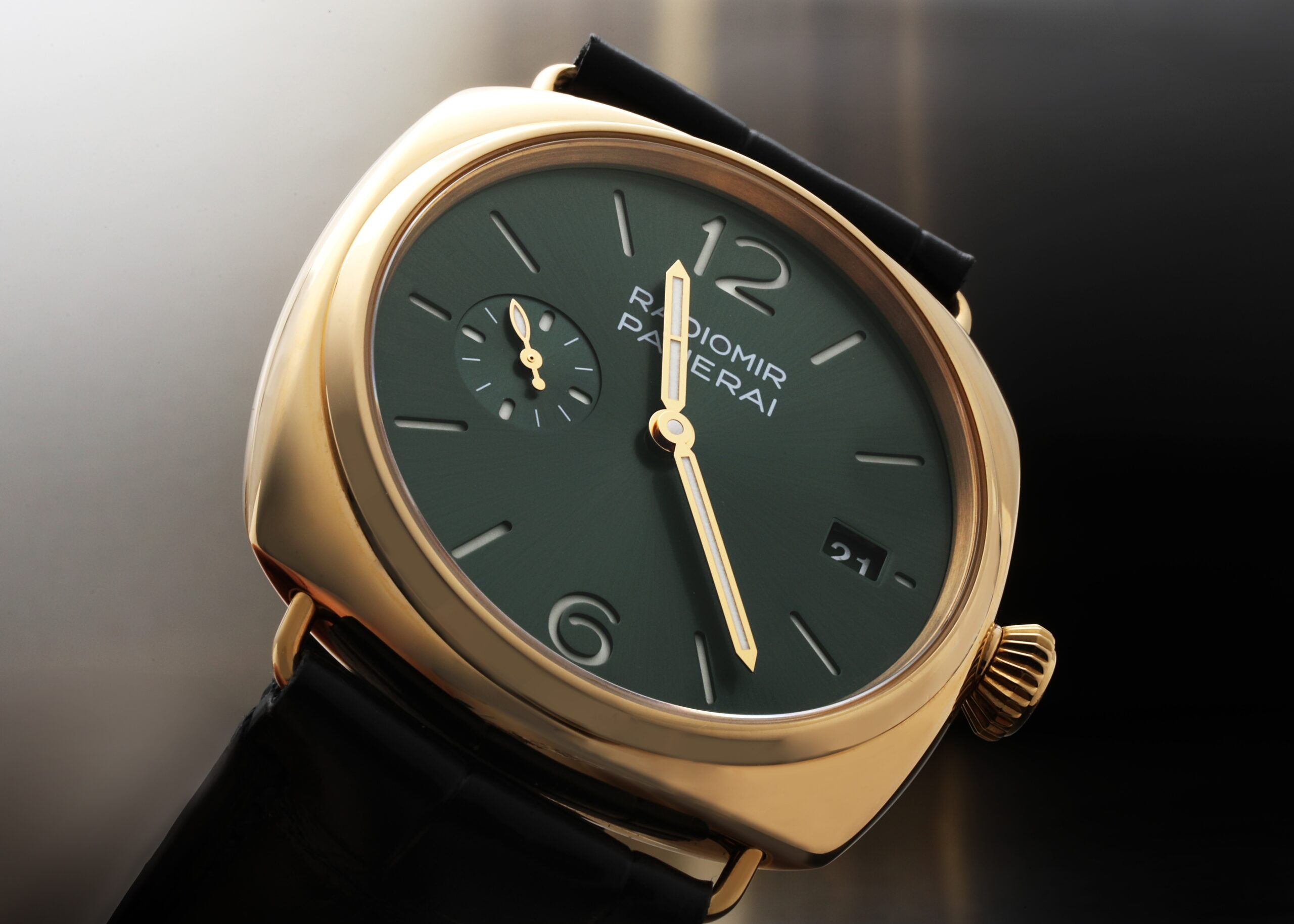A close-up, angled shot of a Panerai Radiomir Quaranta watch with a yellow gold case, green dial, and black leather strap.