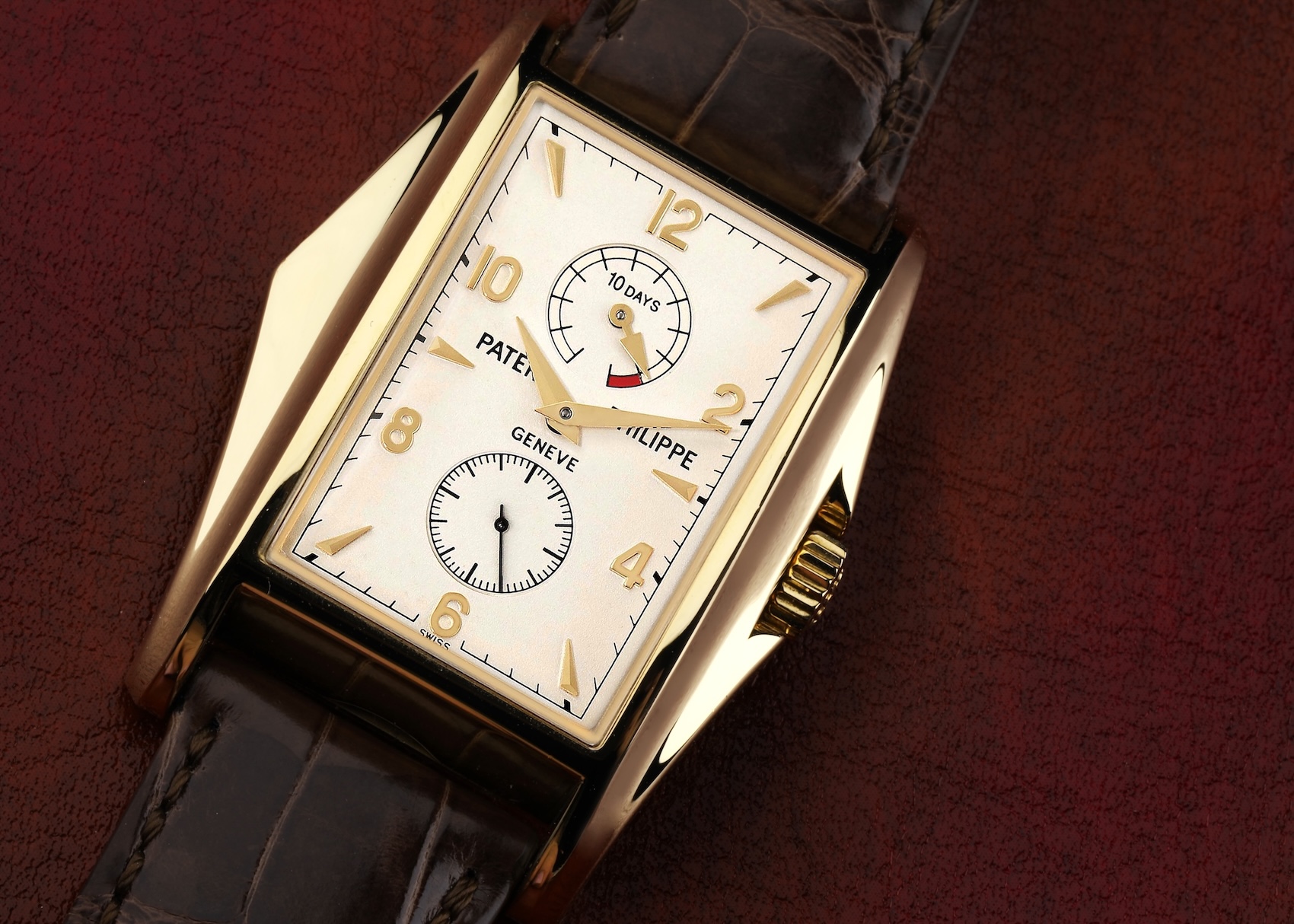 A Patek Philippe 10 Day Power Reserve watch, reference 5100J, on a brown leather background. It has a distinctive rectangular yellow gold case, an off-white dial with a power reserve indicator at 12 o'clock, and a small seconds subdial at 6.