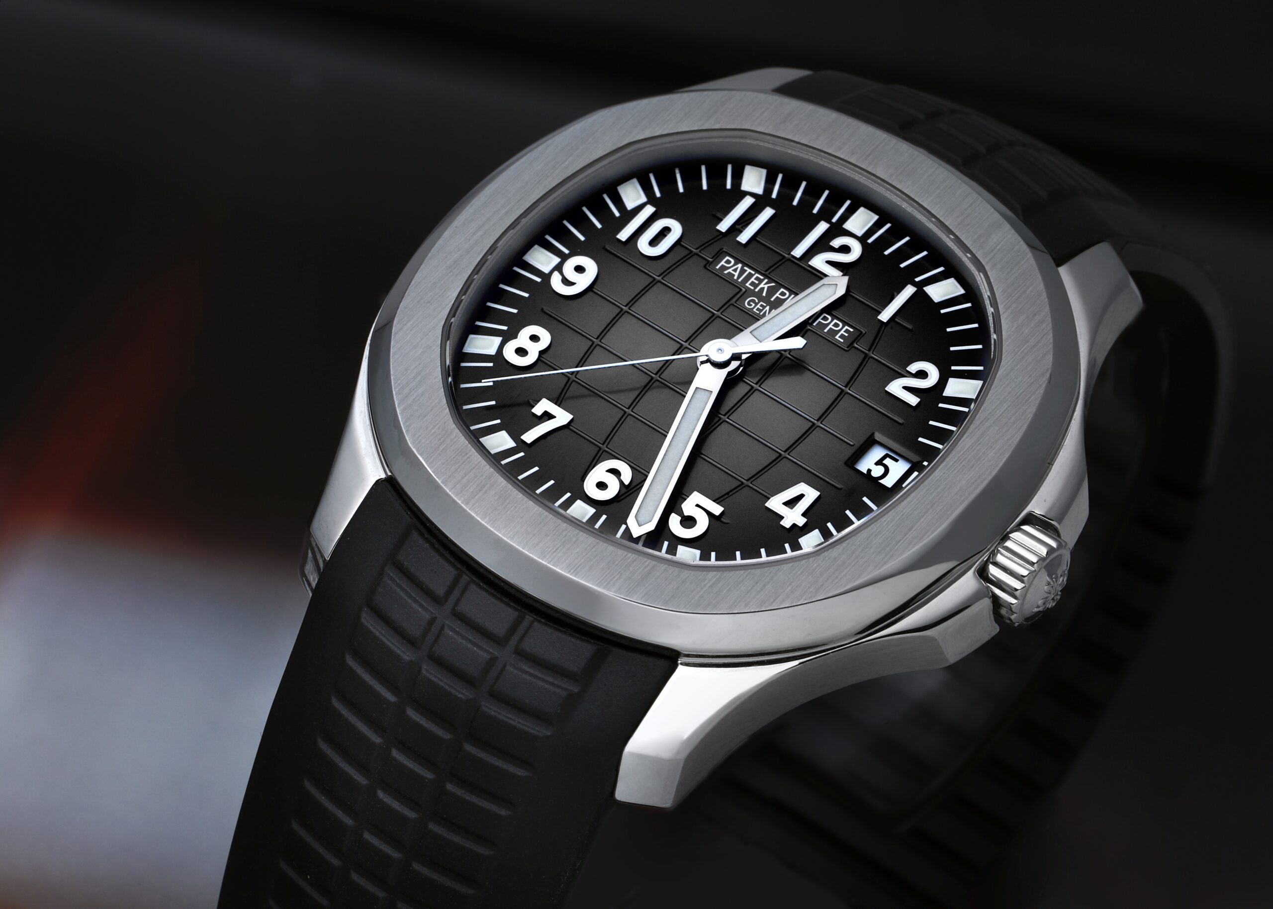 Close-up of a Patek Philippe Aquanaut watch with a black embossed dial, white numerals, and a black rubber strap.