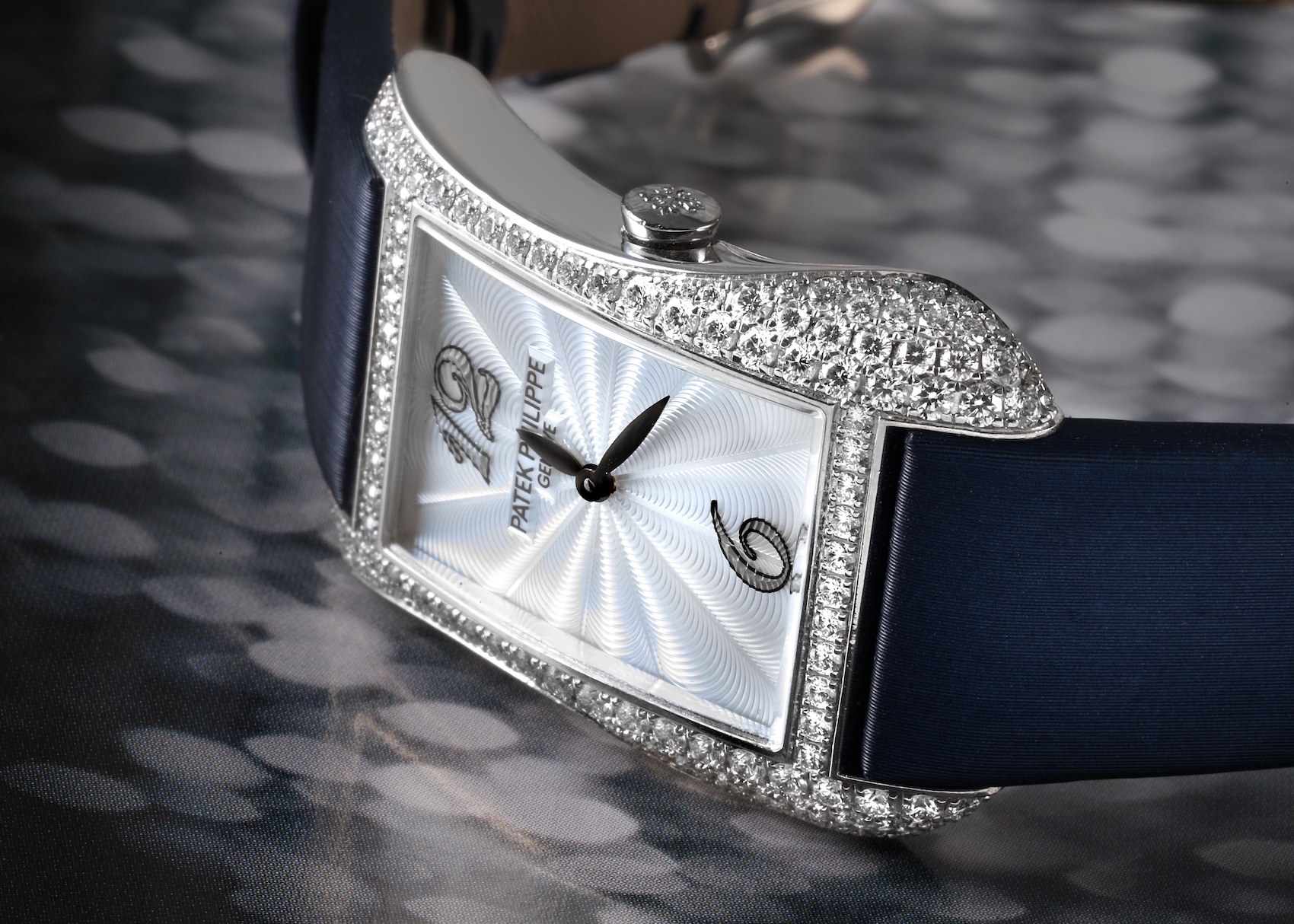 The Patek Philippe Gondolo ladies' watch, featuring a curved, diamond-paved white gold case, a guilloché dial with artistic numerals, and a blue satin strap.