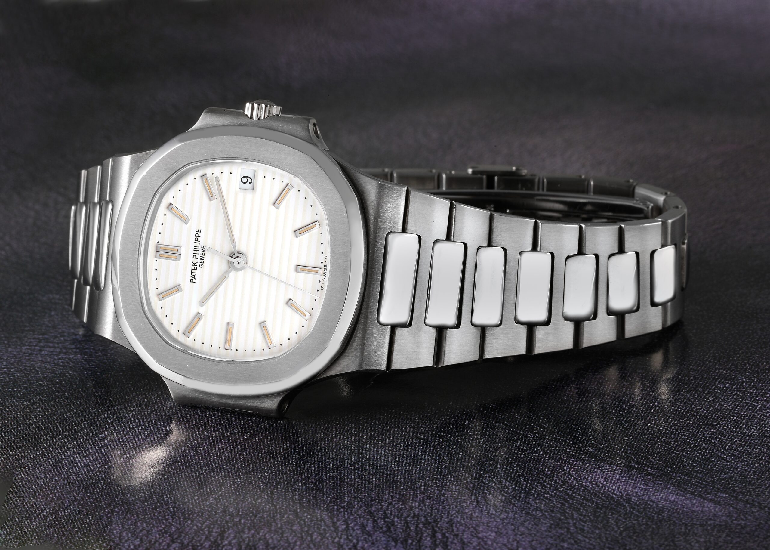 A Patek Philippe Nautilus watch in stainless steel, featuring its distinctive porthole-shaped case and a horizontal striped white dial.