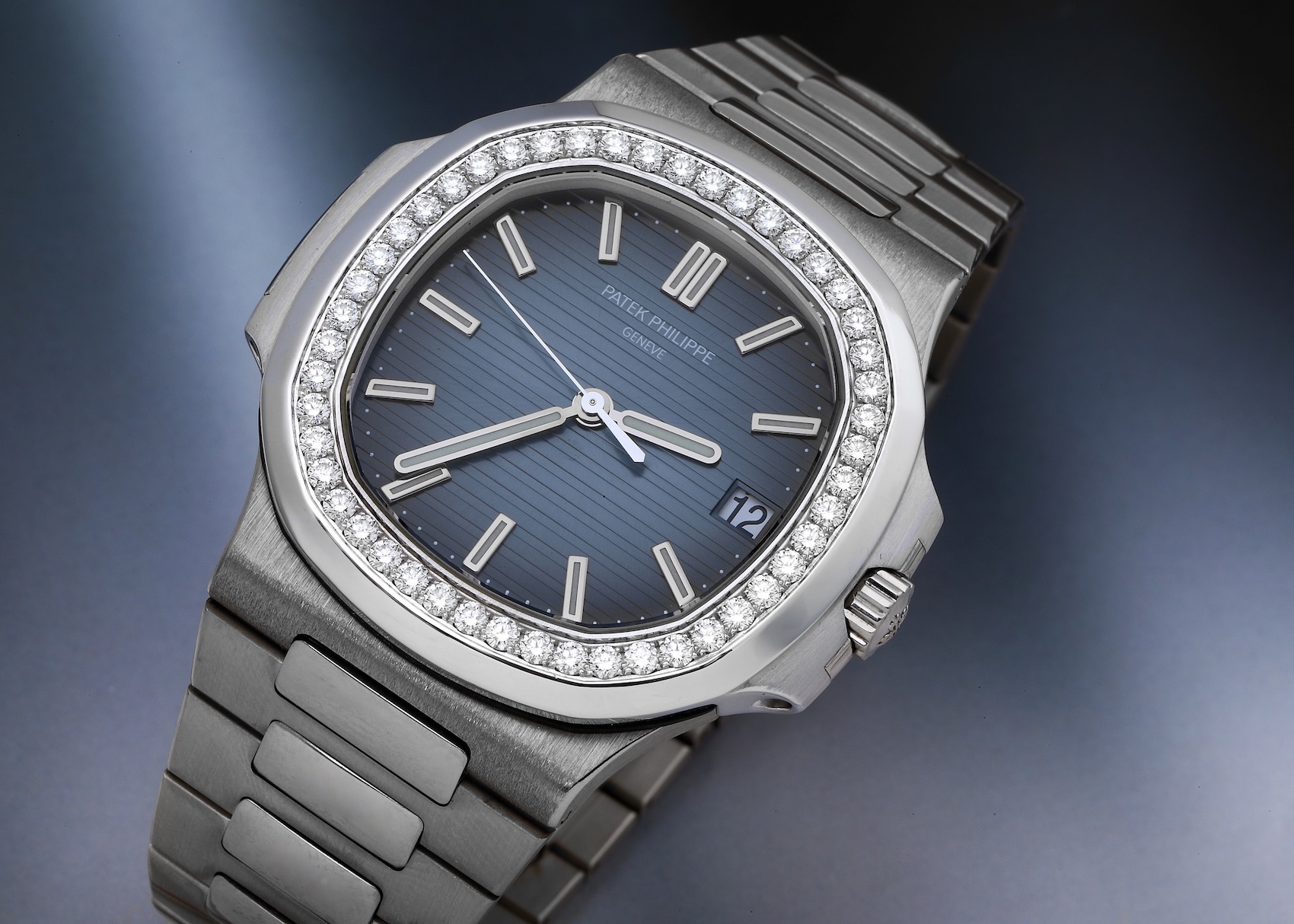 A Patek Philippe Nautilus in white gold, reference 5713, with a factory-set diamond bezel. The watch has the signature porthole-shaped case, a horizontally grooved blue-gray dial, a date window, and an integrated white gold bracelet.