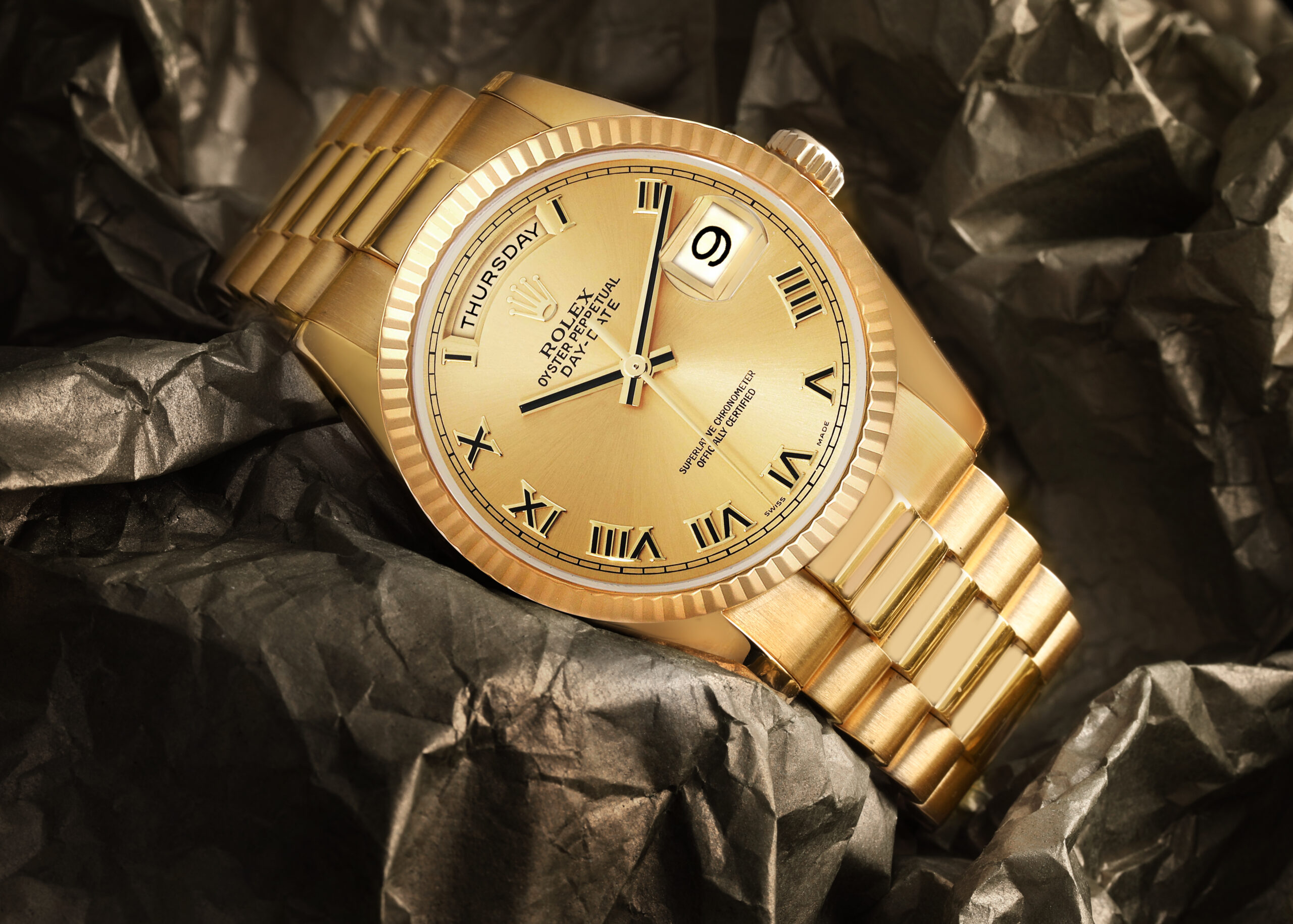 A classic all-yellow-gold Rolex Day-Date with a champagne dial, photographed on a dark, textured surface to highlight its Roman numerals, including "IIII".