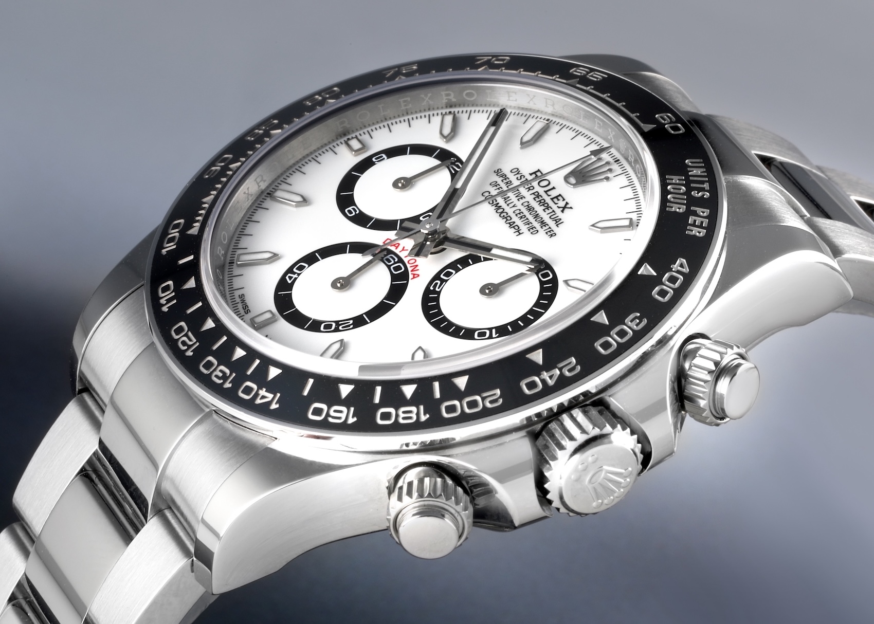An angled close-up of the Rolex Daytona 126500 watch. It features a stainless steel case, a black ceramic tachymeter bezel, a white dial with contrasting black sub-dials, and the iconic Oyster bracelet.