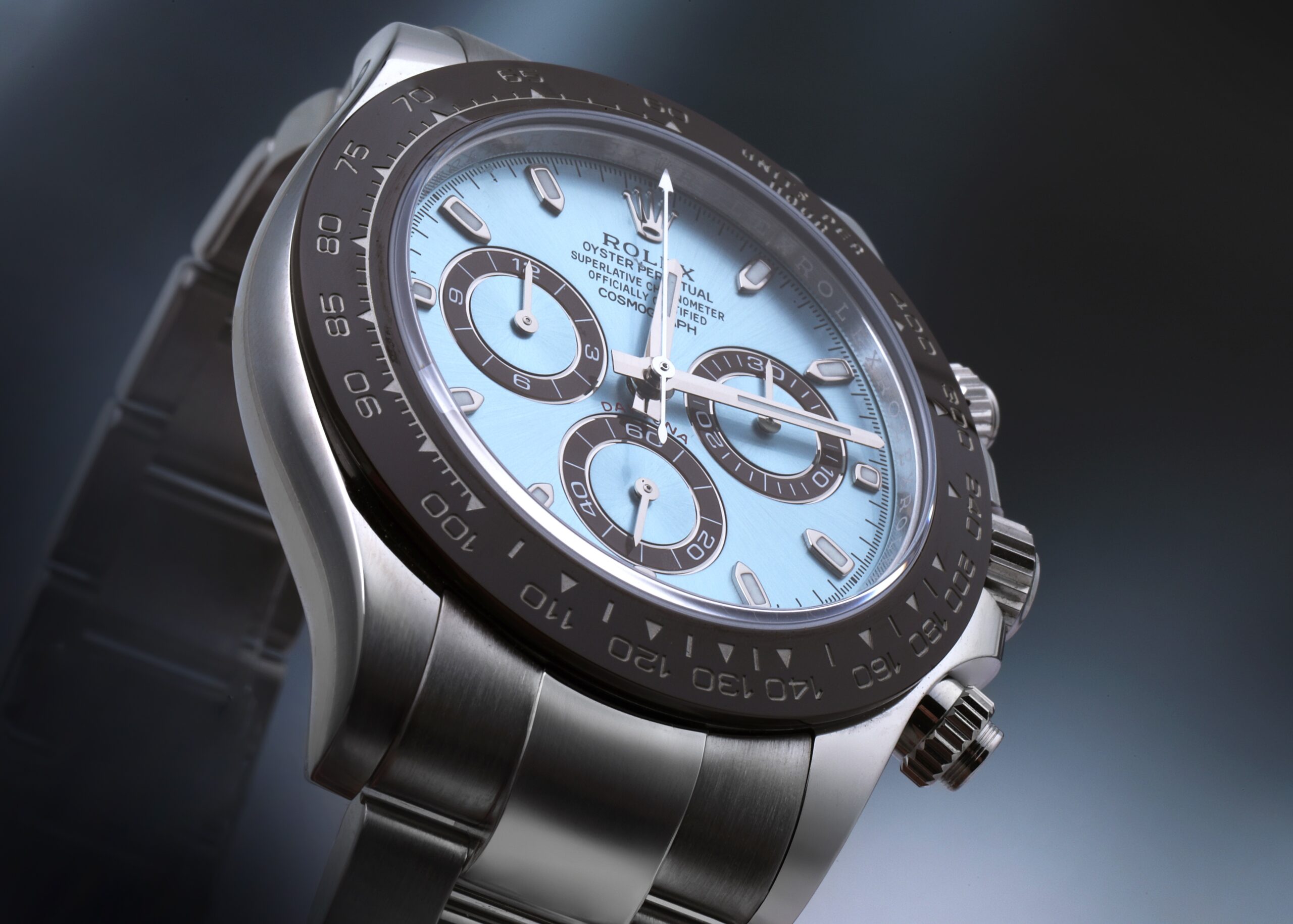Angled view of a Rolex Cosmograph Daytona in platinum with an ice blue dial, baton markers, and a brown ceramic bezel on a stand.