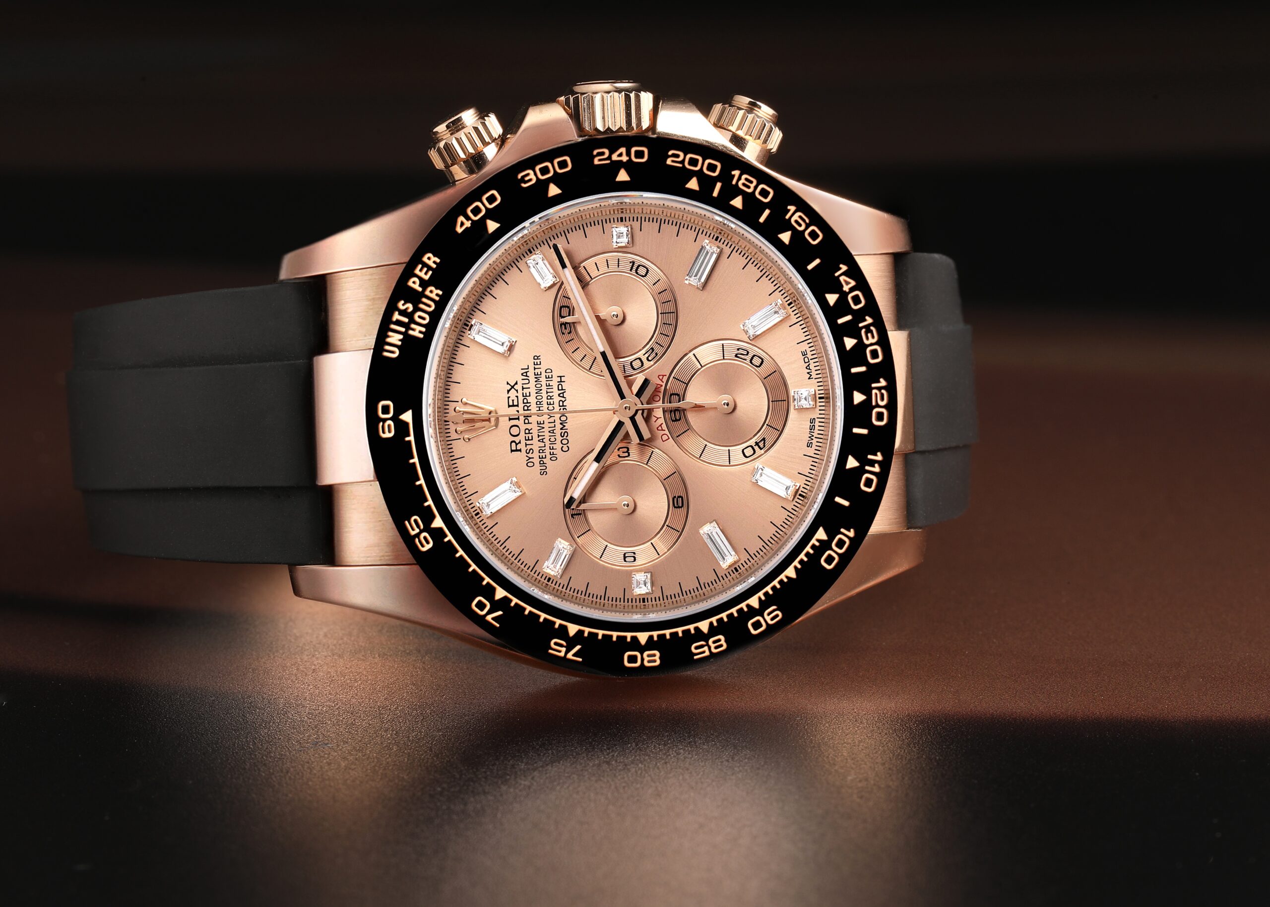 Rolex Cosmograph Daytona watch in rose gold with a black ceramic bezel, Sundust dial, diamond hour markers, and a black Oysterflex rubber bracelet.