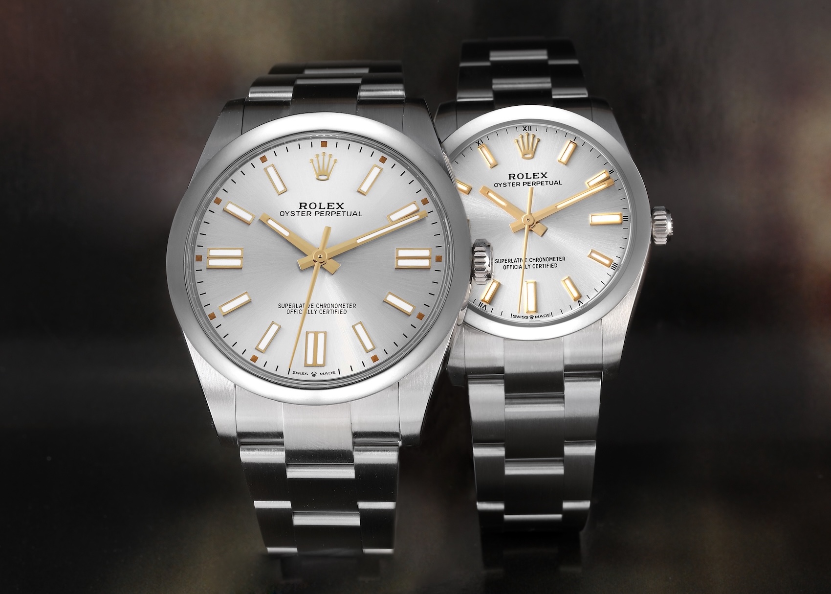 Two Rolex Oyster Perpetual watches, a larger 41mm and a smaller 36mm model, shown side by side. Both feature stainless steel cases, silver sunray dials with gold-tone hands and hour markers, and steel Oyster bracelets.
