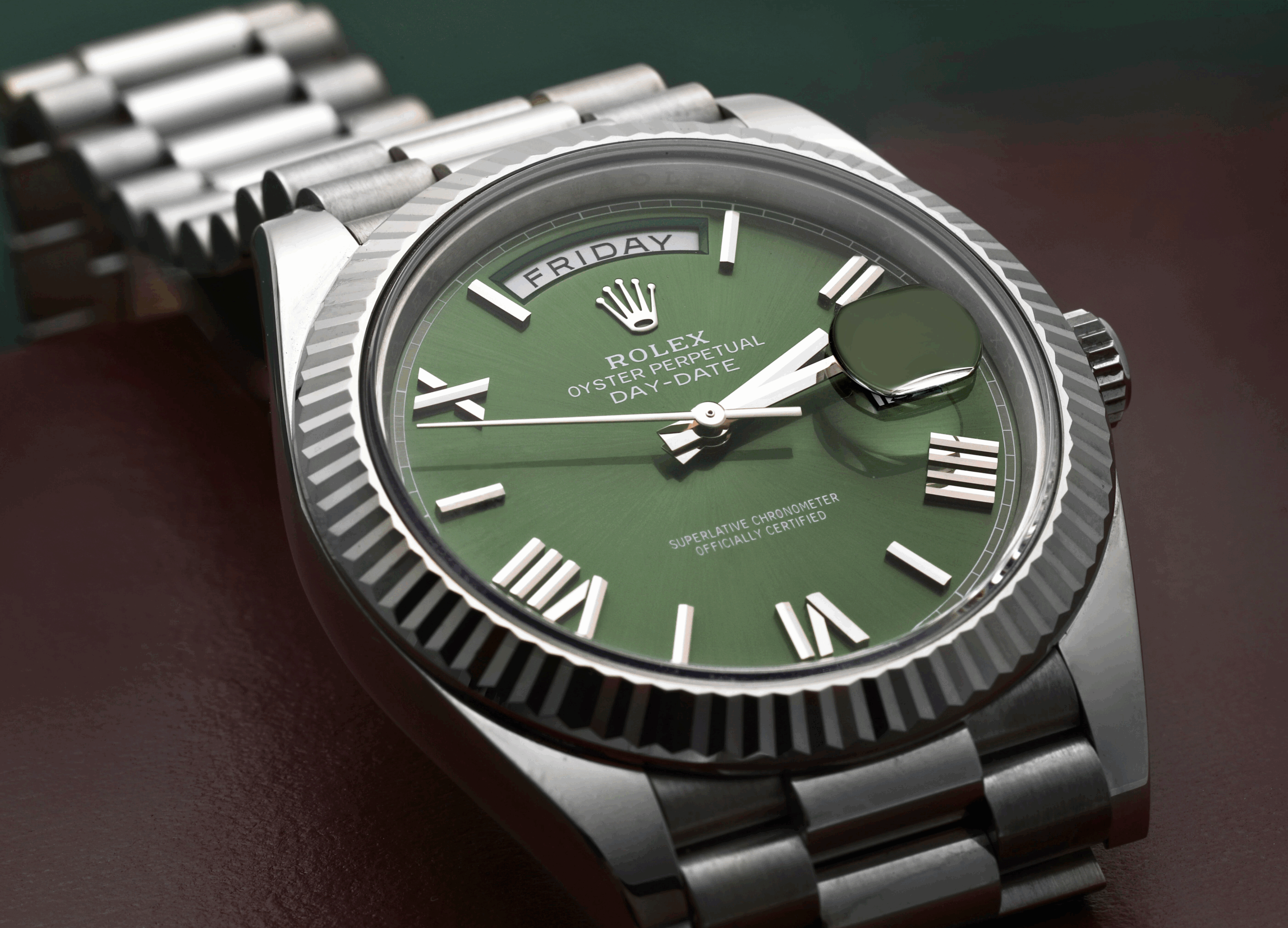 An angled close-up of a Rolex Day-Date with a popular olive green dial and fluted bezel, showcasing its distinctive Roman numeral hour markers.