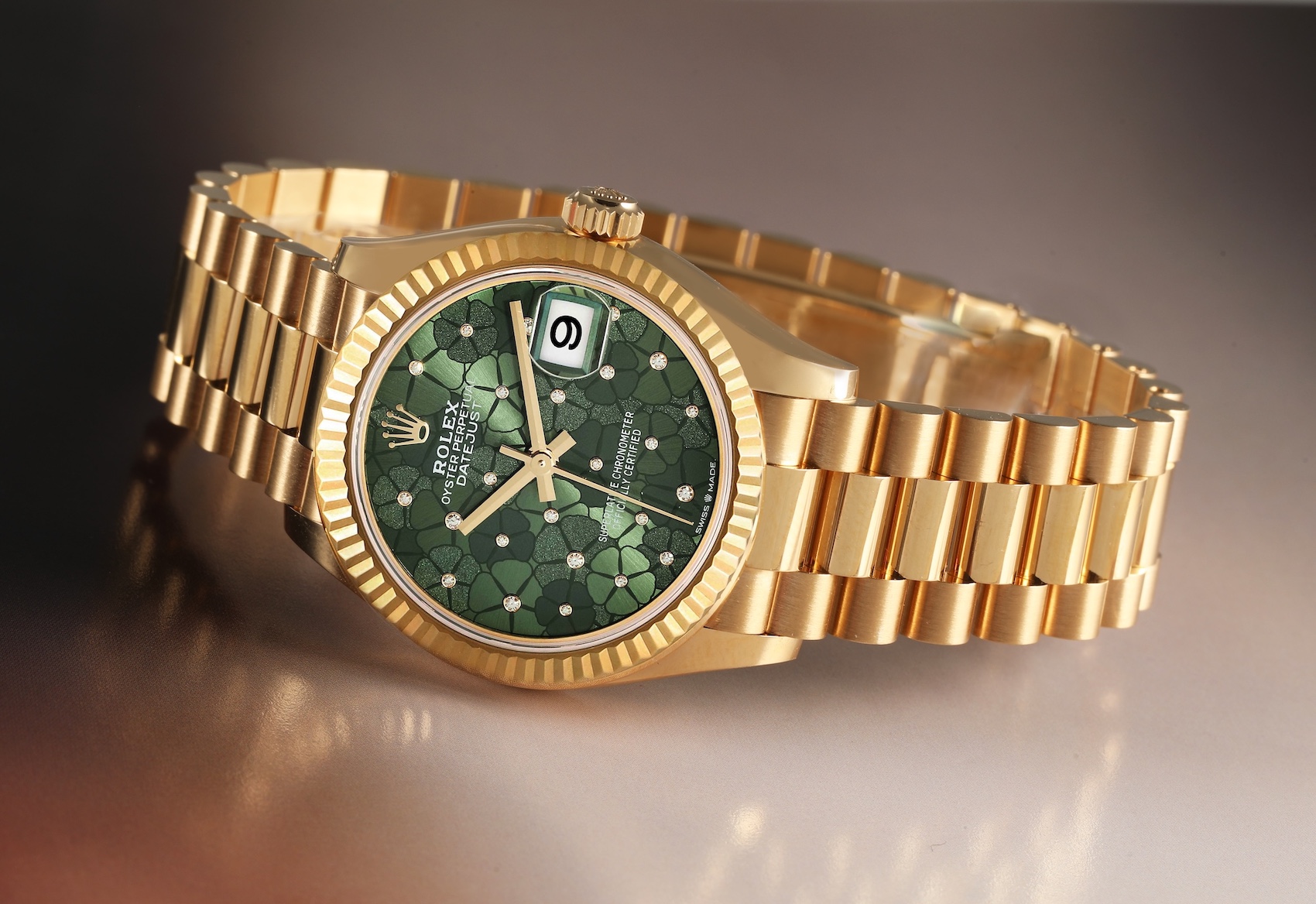 A midsize Rolex Datejust in solid yellow gold on a President bracelet, featuring an intricate dark green floral-motif dial accented with diamonds.