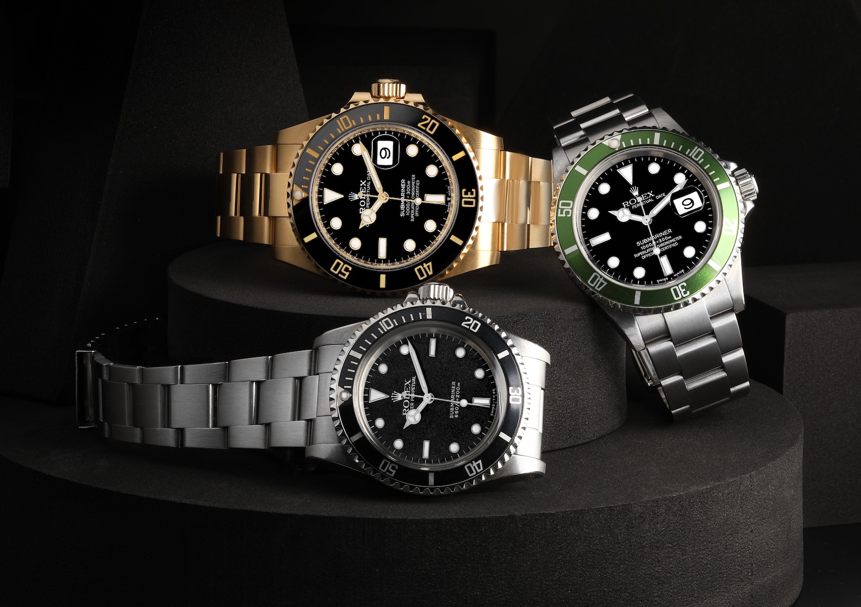 A trio of iconic Rolex Submariner watches including a vintage 5513 in stainless steel, a 16610LV "Kermit" with a green bezel, and a luxurious 126618 in gold.