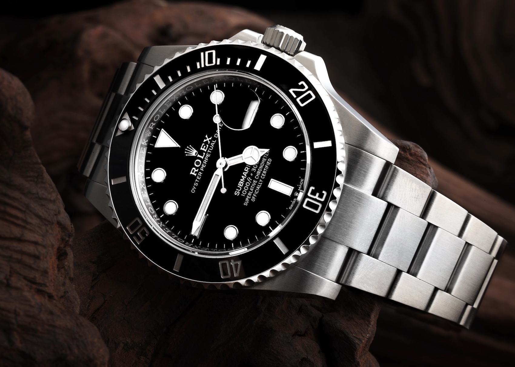 A Rolex Submariner Date 126610 resting on a piece of dark wood. The watch has a stainless steel case, a black dial with luminous markers, a black ceramic unidirectional bezel, and a steel Oyster bracelet.