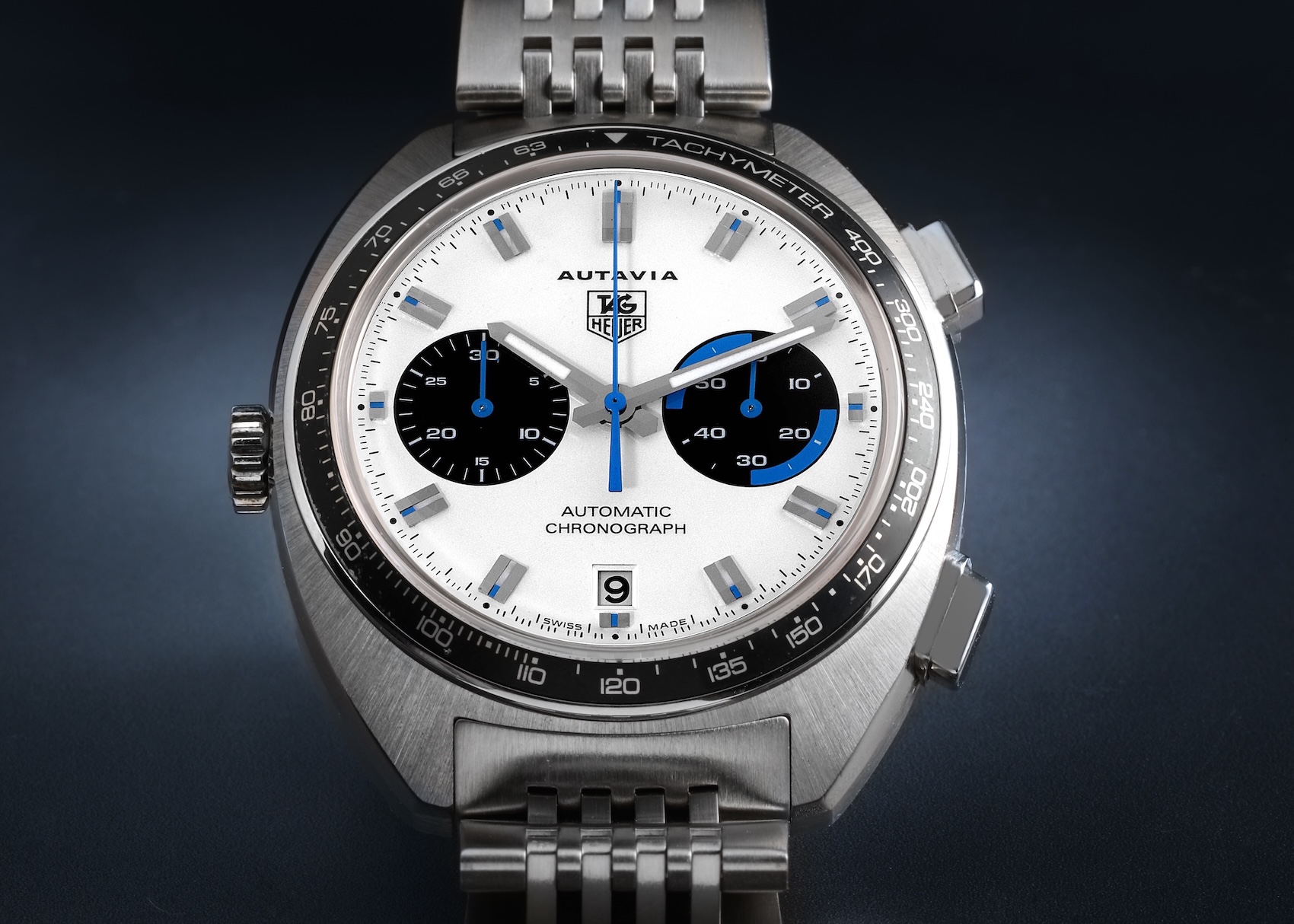 A front-facing view of a Tag Heuer Autavia Automatic Chronograph. It has a cushion-shaped stainless steel case, a white 'panda' dial with two black subdials, blue accents, and a steel bracelet.
