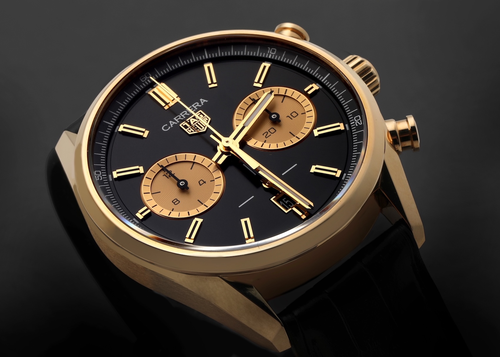 An elegant Tag Heuer Carrera chronograph in yellow gold. The watch has a black dial with gold-tone hands, hour markers, and two contrasting subdials, paired with a black alligator leather strap.