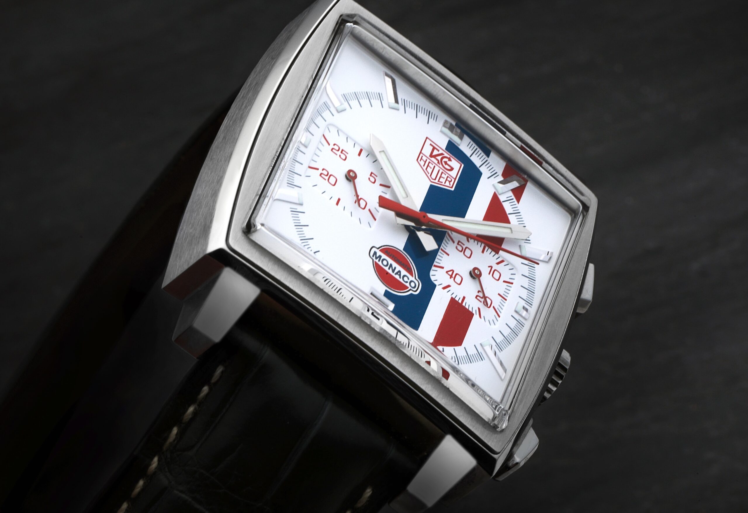 A close-up of the TAG Heuer Monaco CW2118, the "McQueen" limited edition, showing its white dial with iconic red and blue racing stripes.
