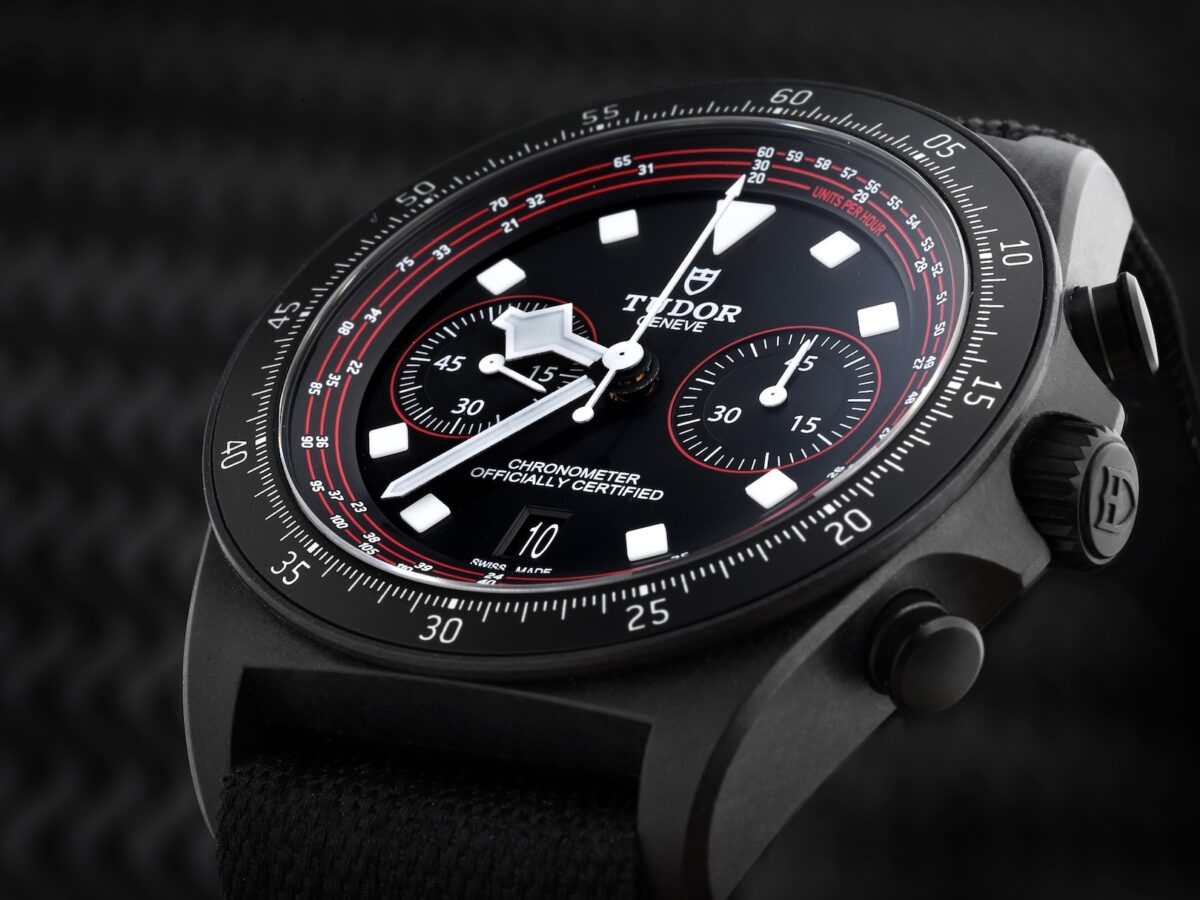 A close-up side profile of the Tudor Pelagos FXD Chrono Cycling Edition, highlighting the matte finish of the carbon case, the prominent winding crown, and the black fabric strap.