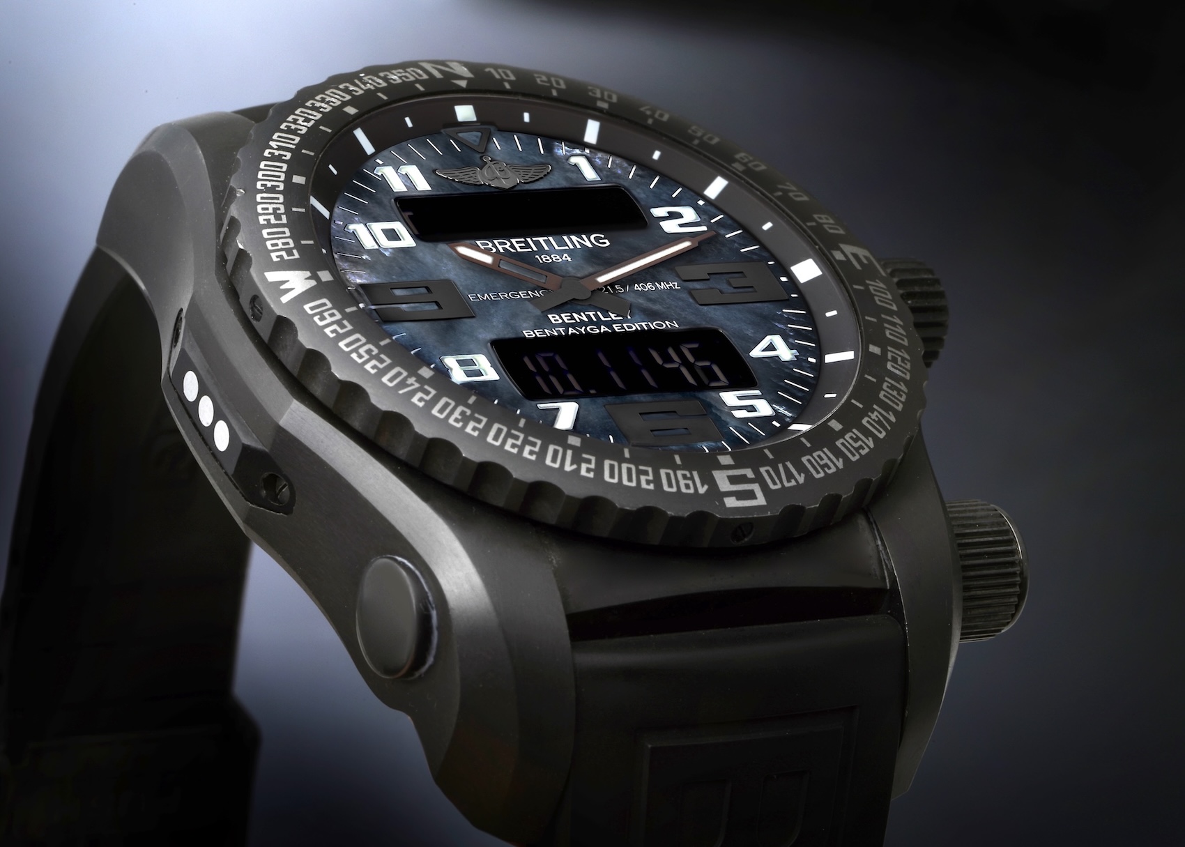 A close-up of the Breitling Emergency II Night Mission watch, showing its black titanium case, dark mother-of-pearl dial with large Arabic numerals, and a digital display window.