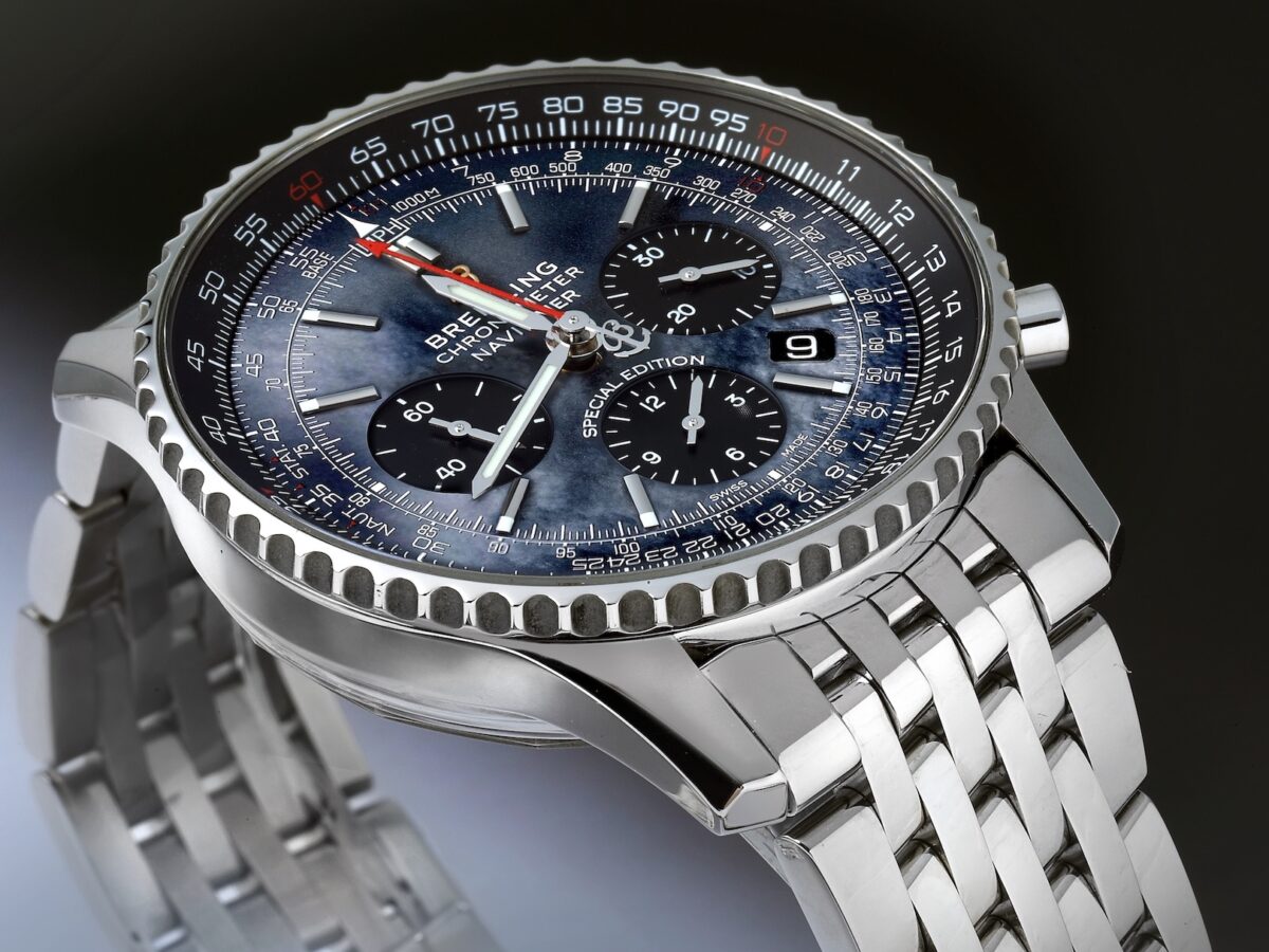 A close-up, angled shot of a Breitling Navitimer 01 watch featuring a stunning blue mother-of-pearl dial with black subdials, a steel case, and a multi-link steel bracelet.